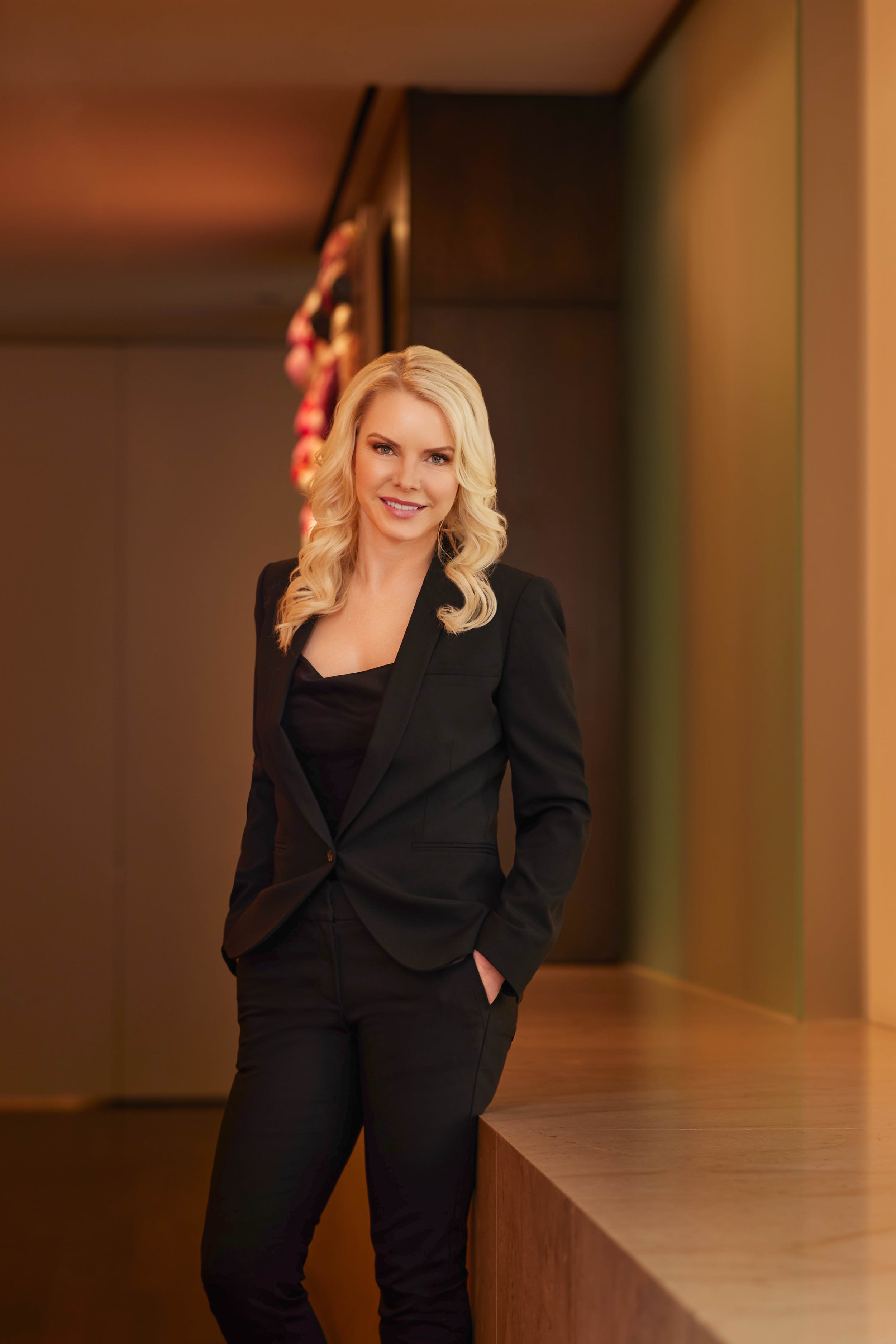 Professional three-quarter portrait of a woman in a black blazer photographed in a modern interior.
