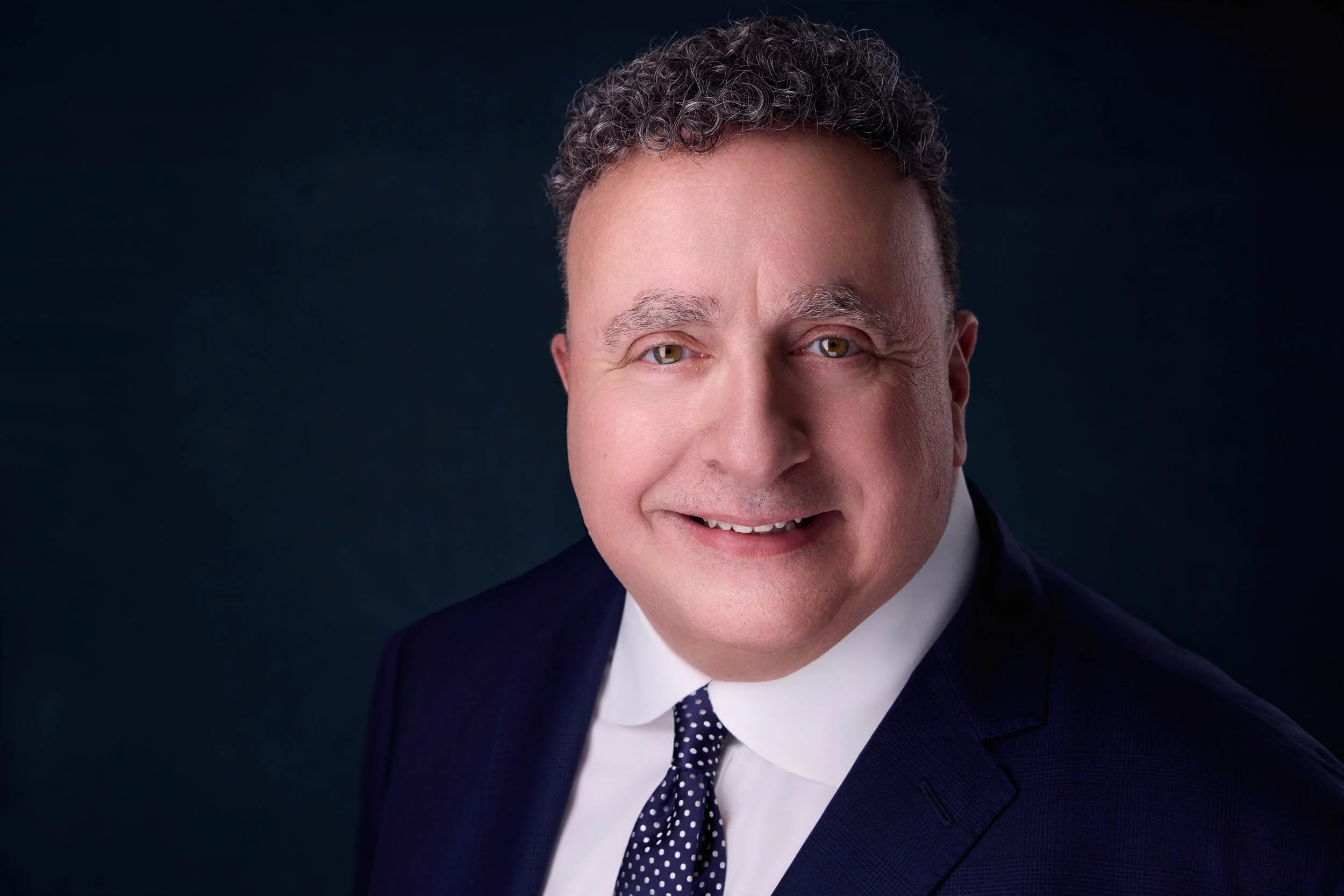 Executive portrait of a man in a dark suit with a confident expression against a deep blue background.