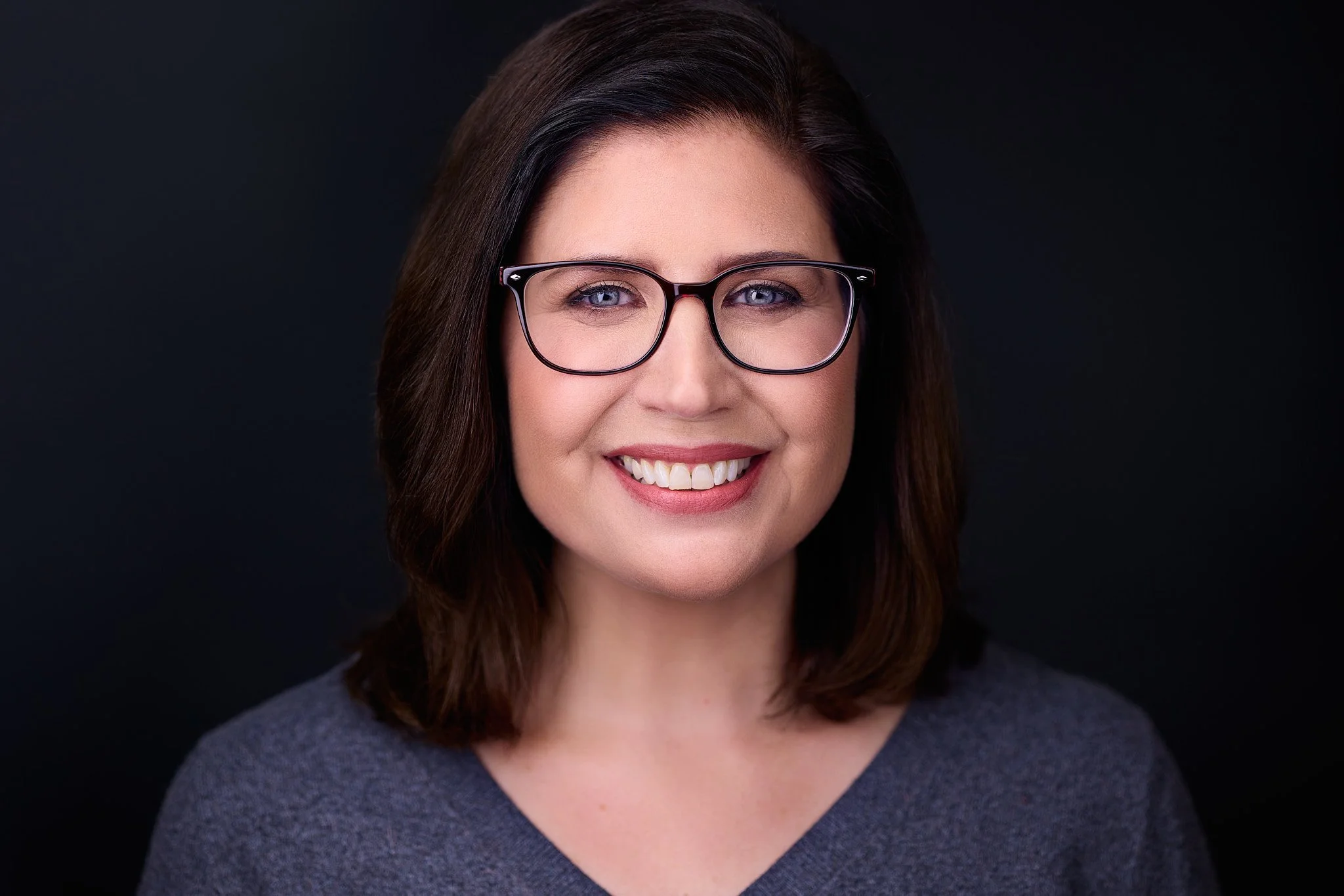 Professional headshot with a warm, engaging expression and glasses.
