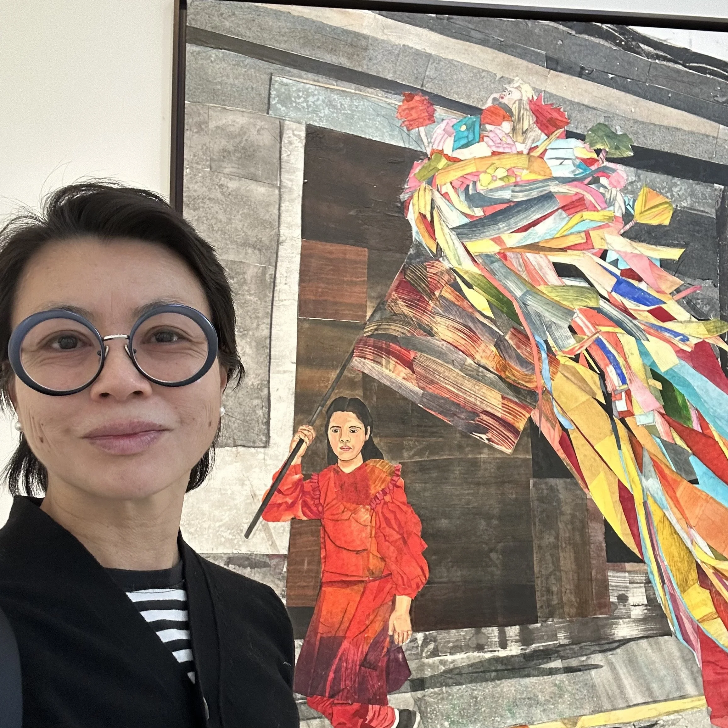 Smiling woman with glasses and short blond hair in a yellow sweater in indoor setting.