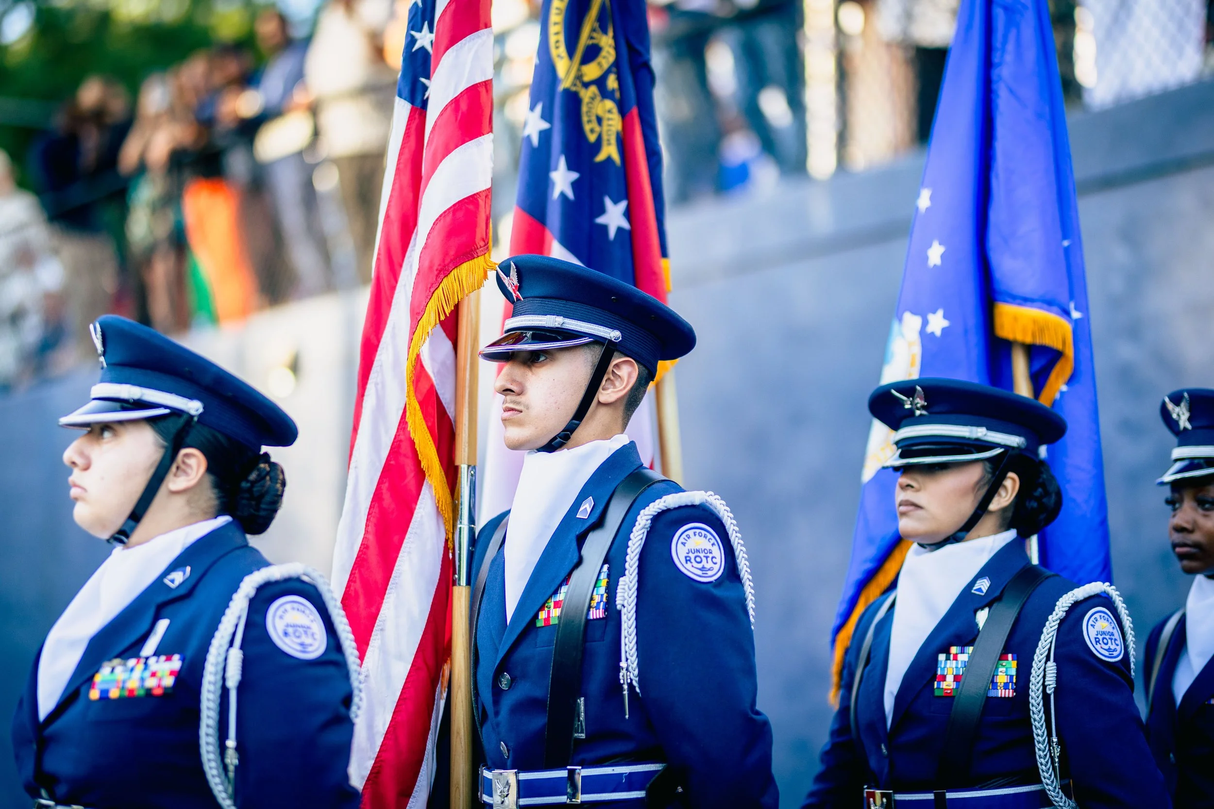 Young female cadets in uniform standing at attention during a flag ceremony, holding American and other flags.