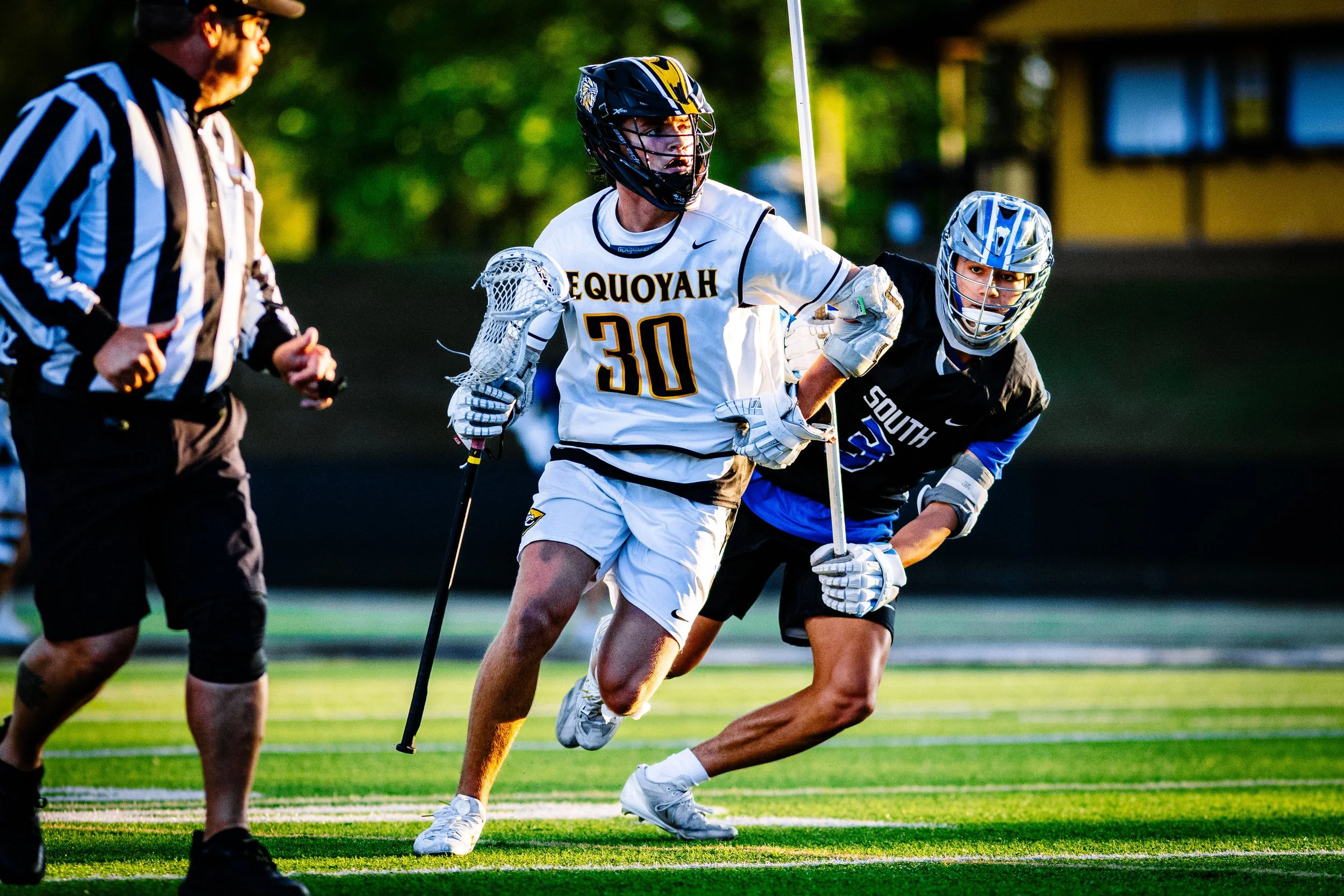 Lacrosse players competing with a referee observing.