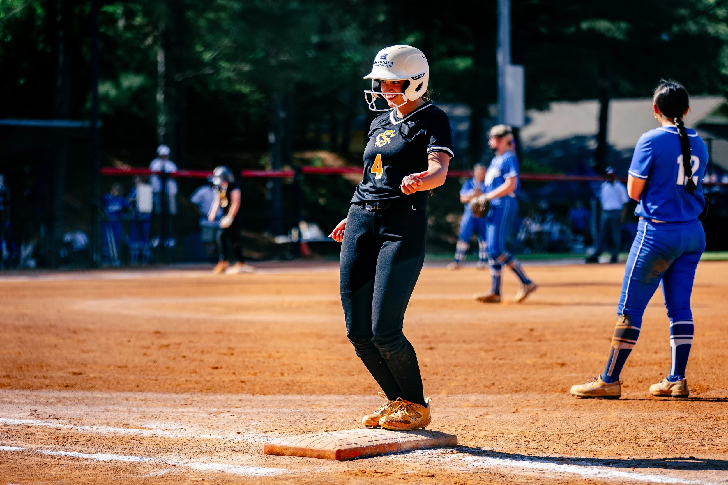 A female softball player in black uniform and helmet standing on first base during a game.