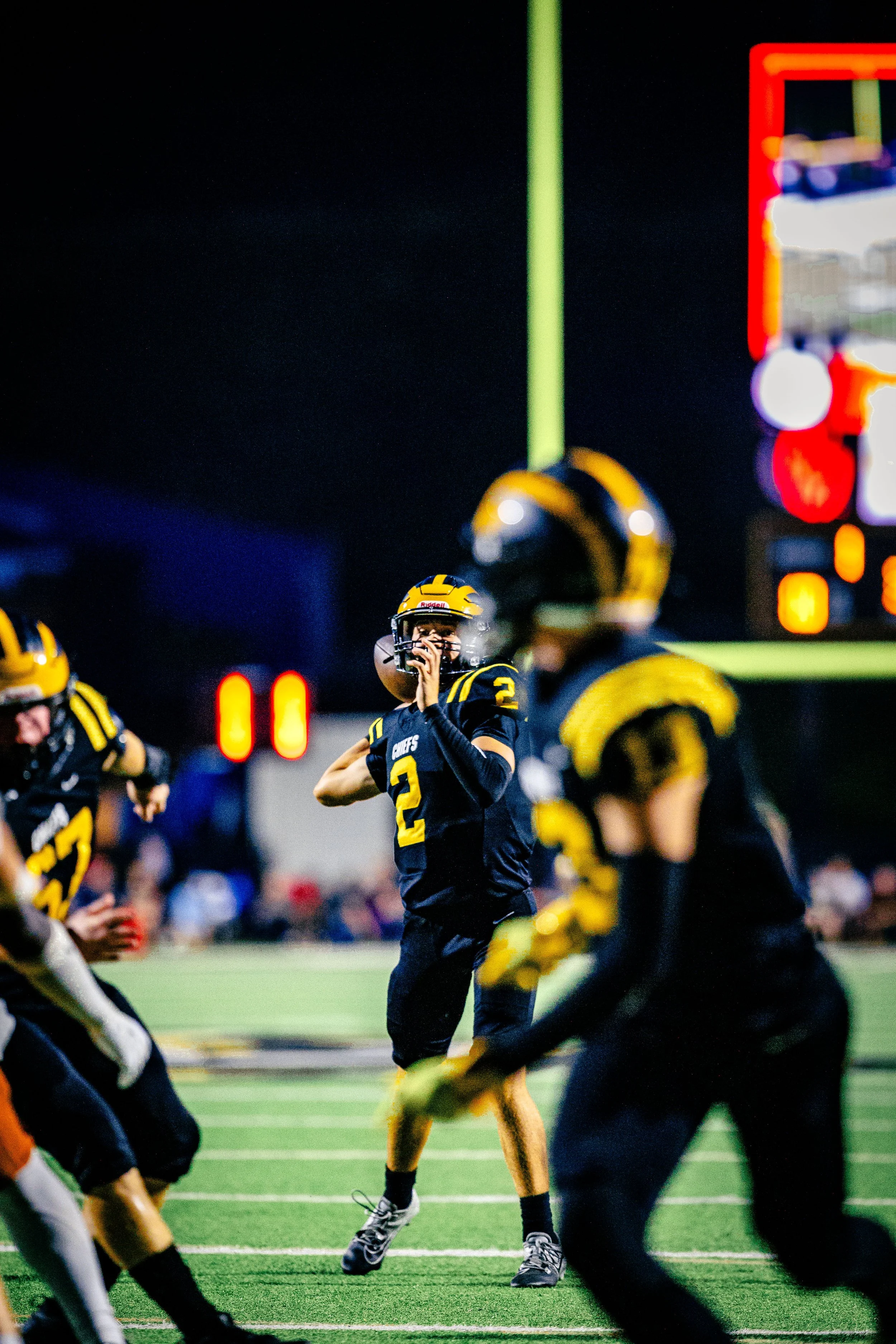 American football players in black and yellow uniforms on the field during a game at night, with one player preparing to throw the ball.