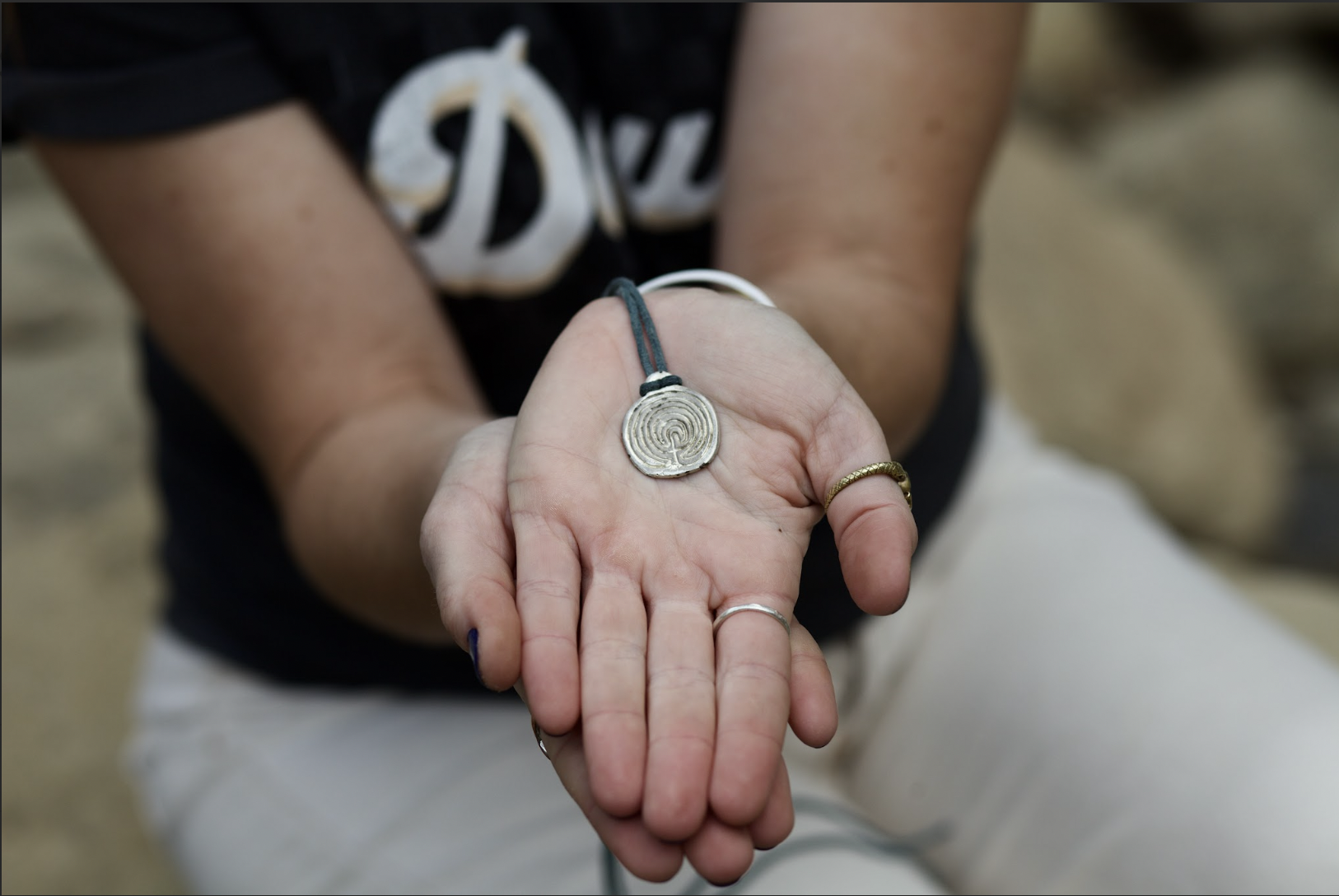 Doula Dyson’s hands extend toward the camera holding a labyrinth necklace. The labyrinth is a silver pendant on a blue suede string. Doula Dyson wears this necklace to all births and prenatal visits.