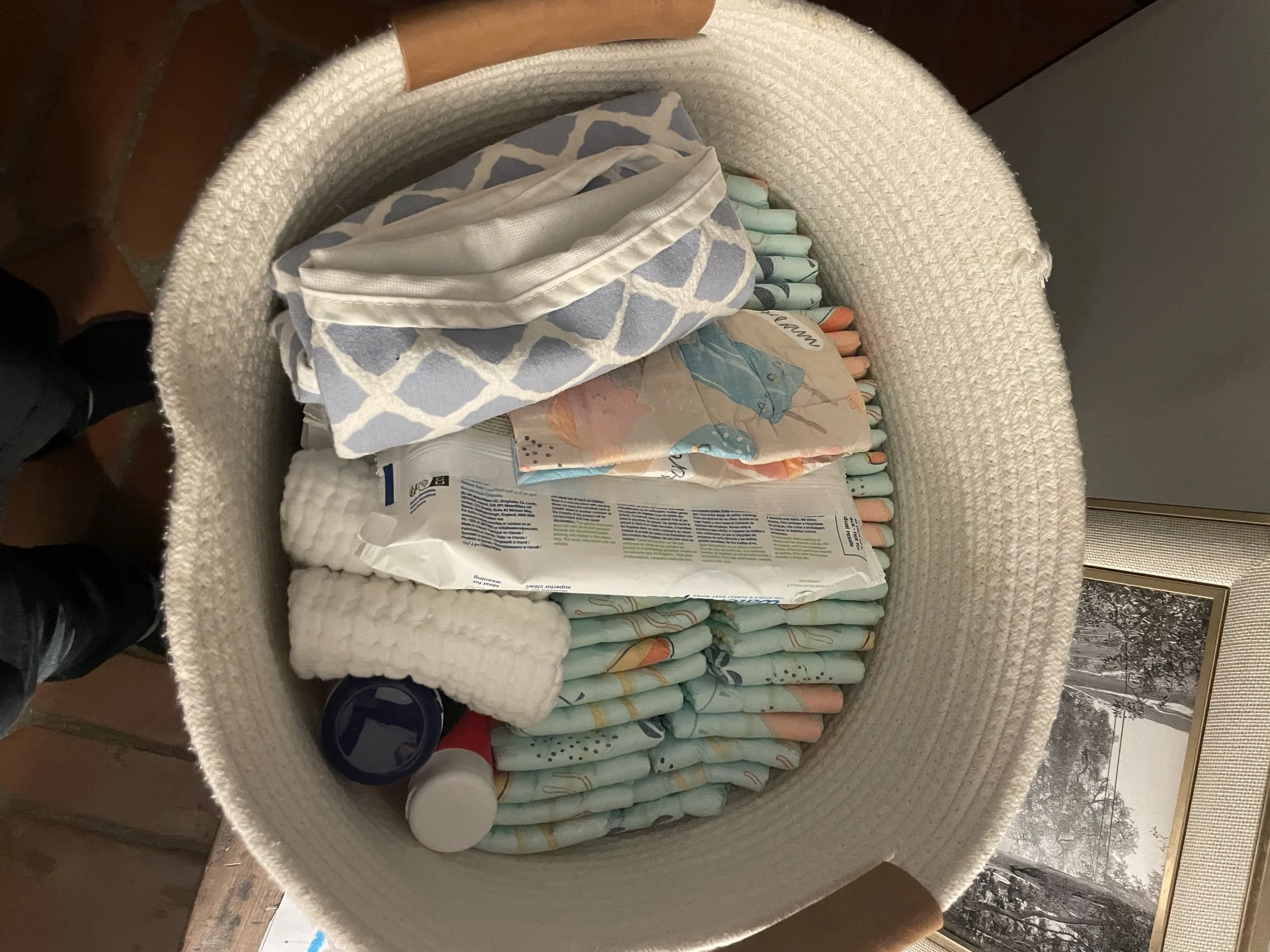 White basket filled with diapers, wipes, changing cloth, burp cloth, and butt dream for overnight postpartum support.