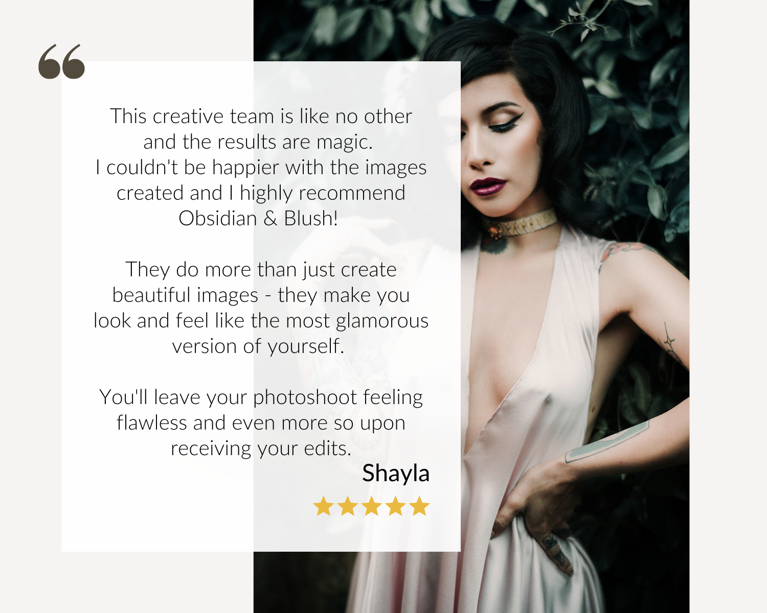 A woman with dark hair and tattoos wearing a light-colored satin dress, standing outdoors next to green foliage.