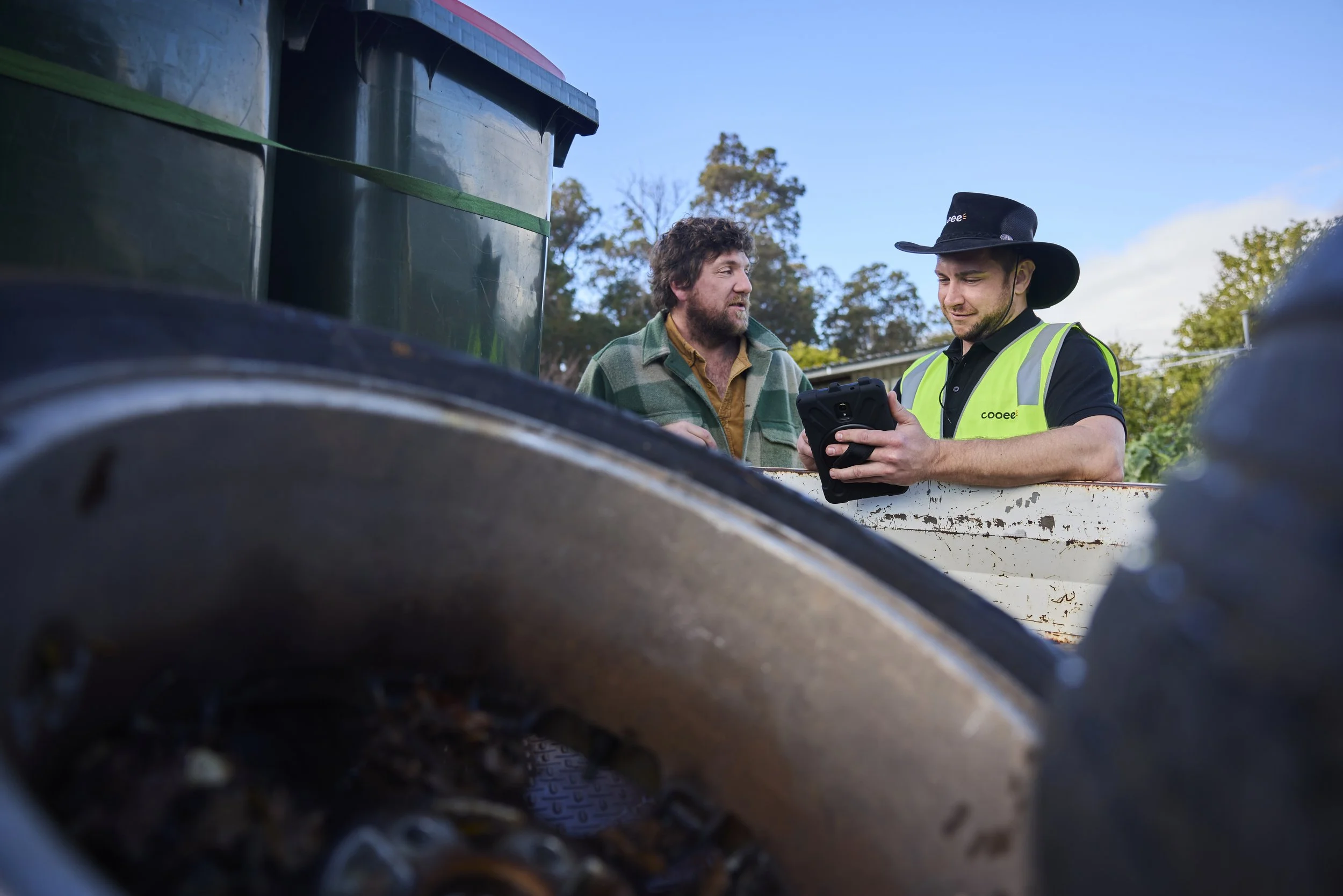 2 men lean over a truck loaded with bins and waste materials