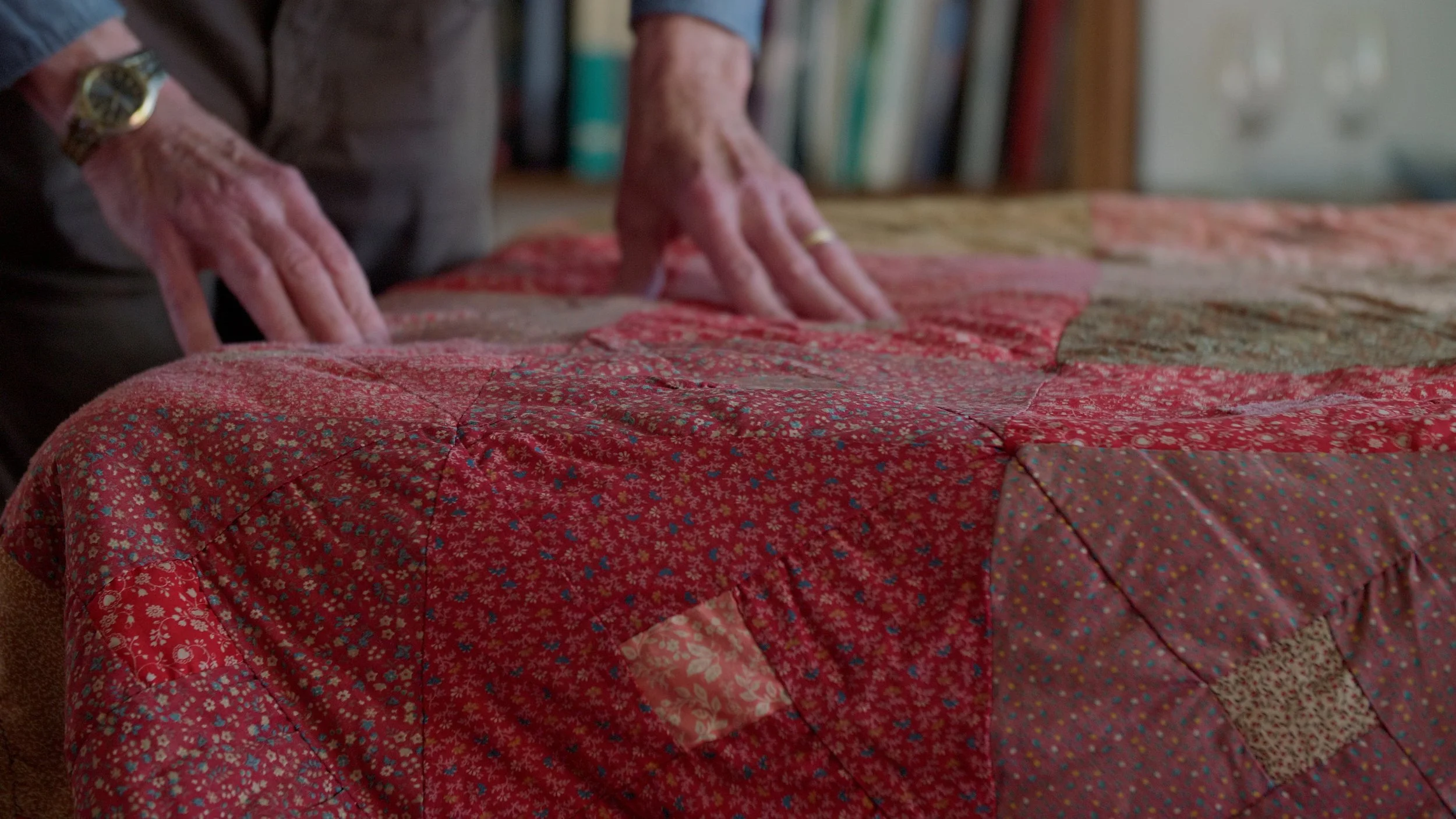 Hands touching a red floral patchwork quilt.