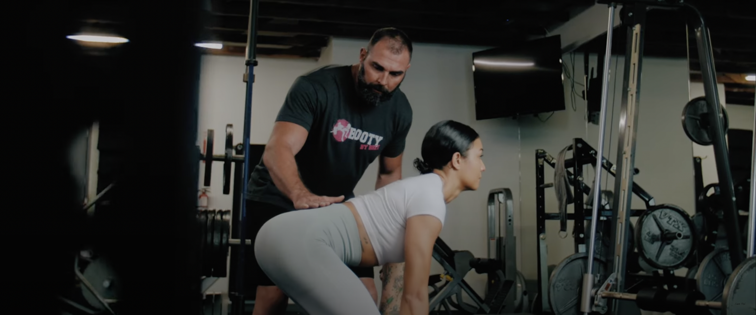 Fitness trainer assisting a woman with exercise in a gym.