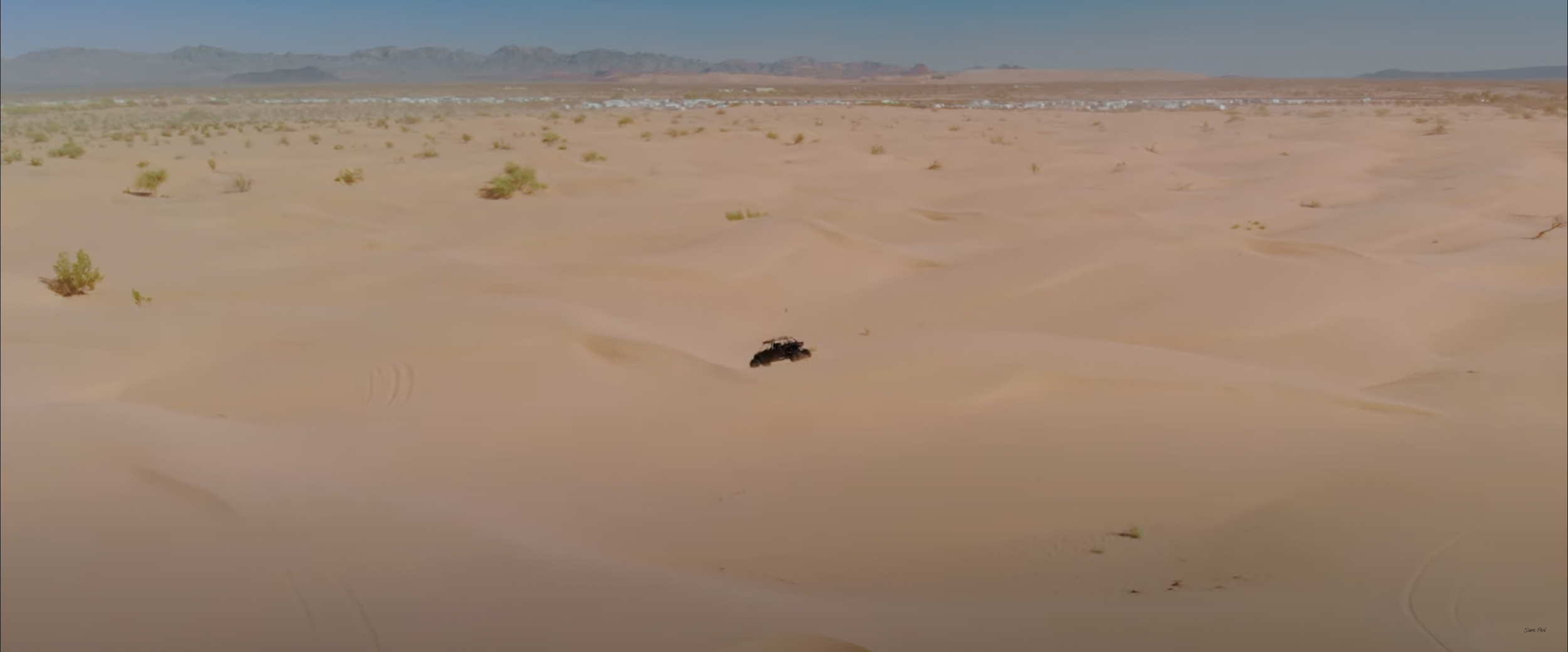 Desert landscape with sand dunes and sparse vegetation under a clear blue sky