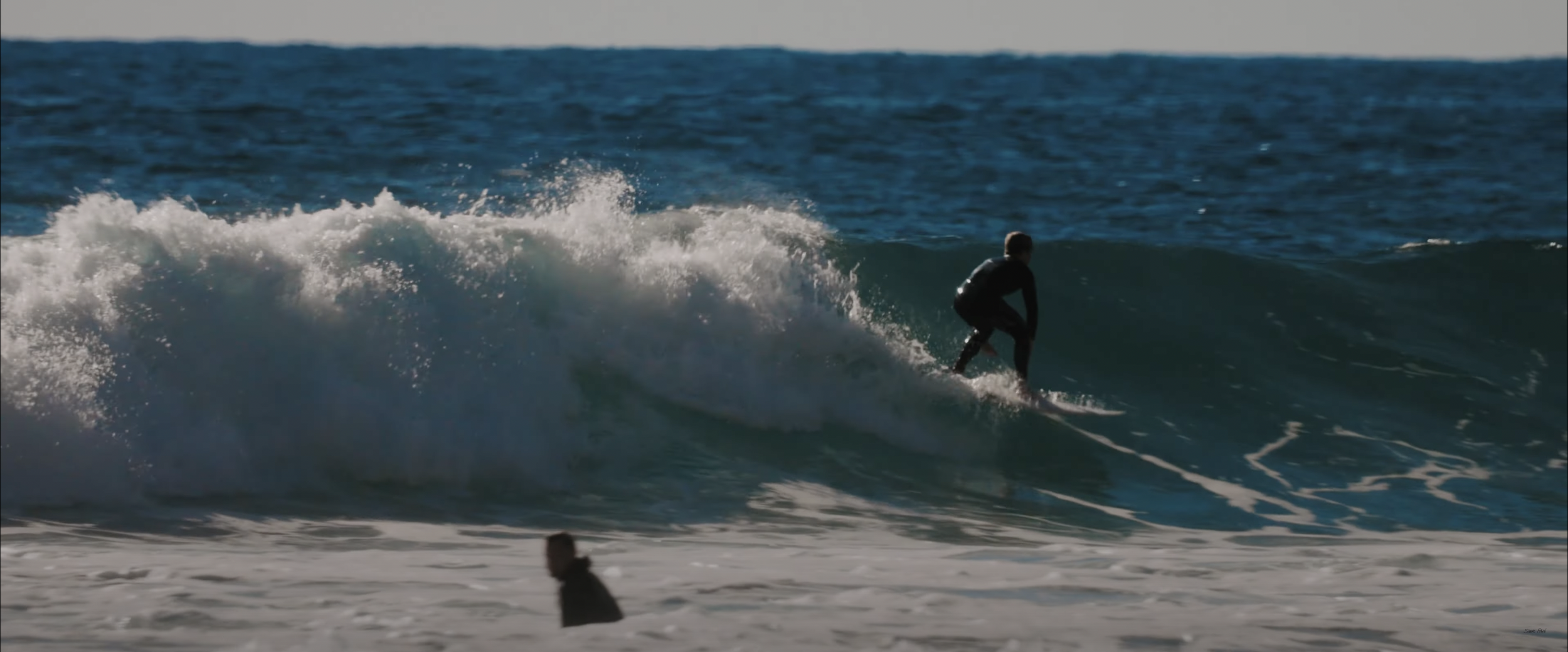 Surfer riding a large ocean wave with another person in the foreground
