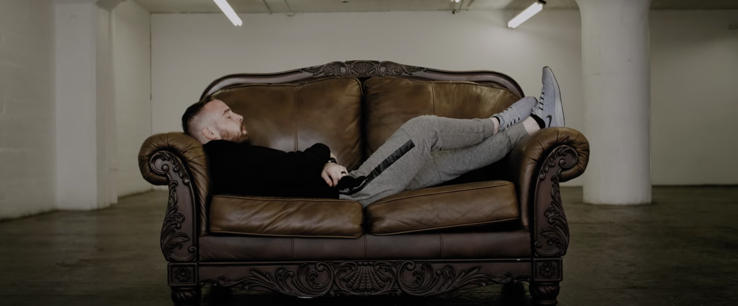 Man lying on brown leather sofa in an empty room