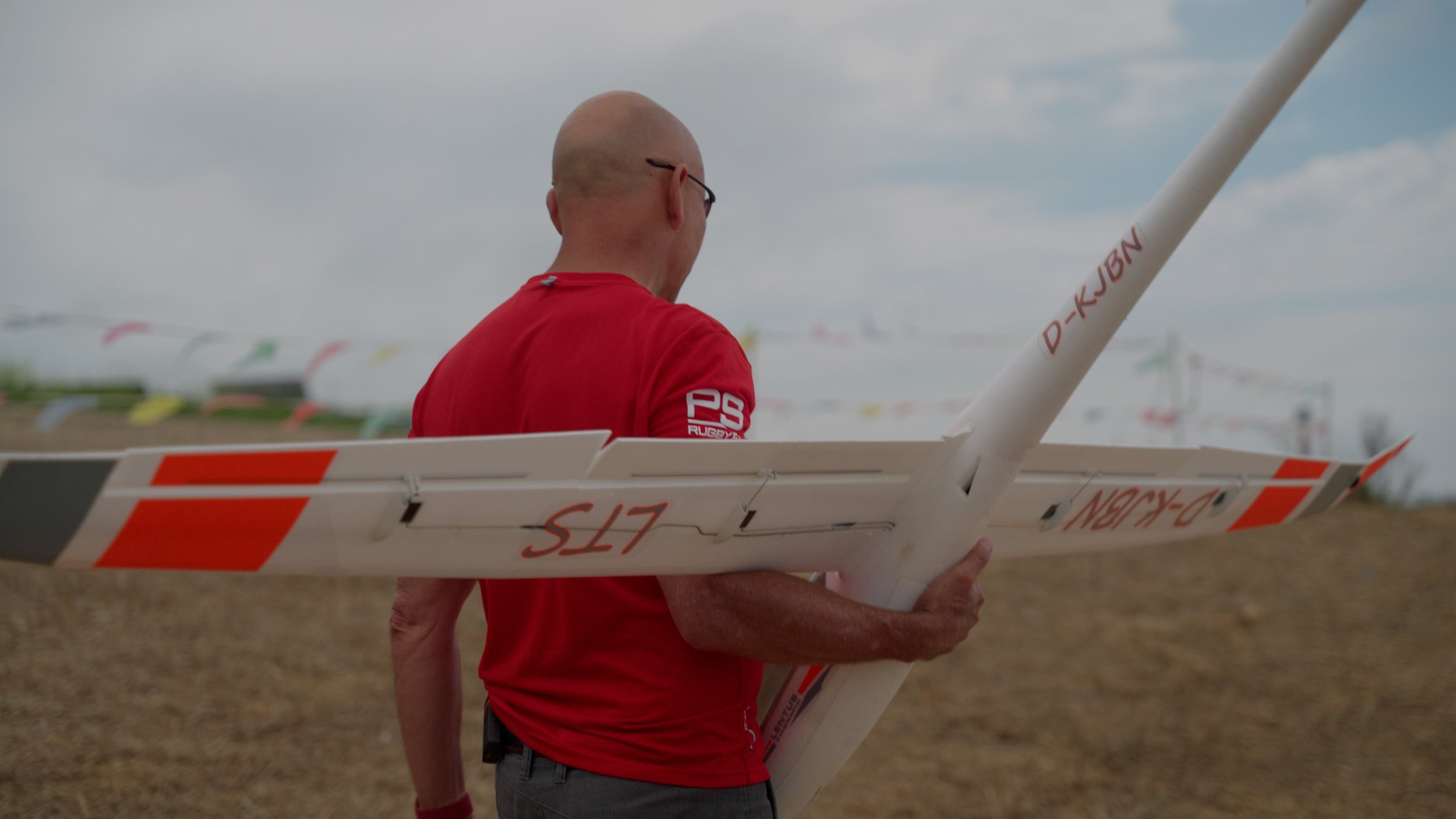 A person in a red shirt holding a white and orange model airplane outdoors.