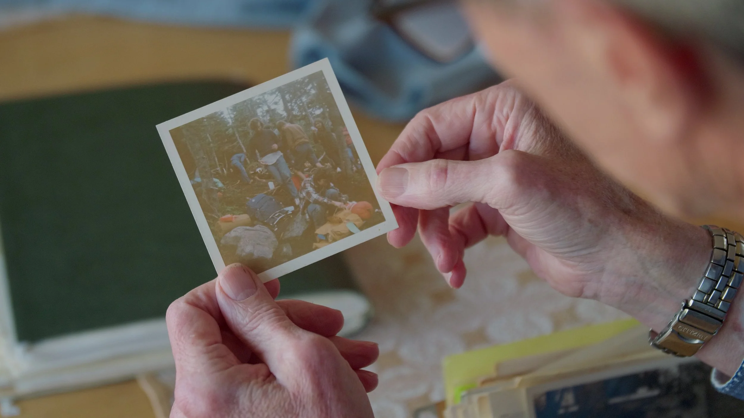Person holding a vintage photograph of a group of people outdoors, surrounded by nature and camping gear.