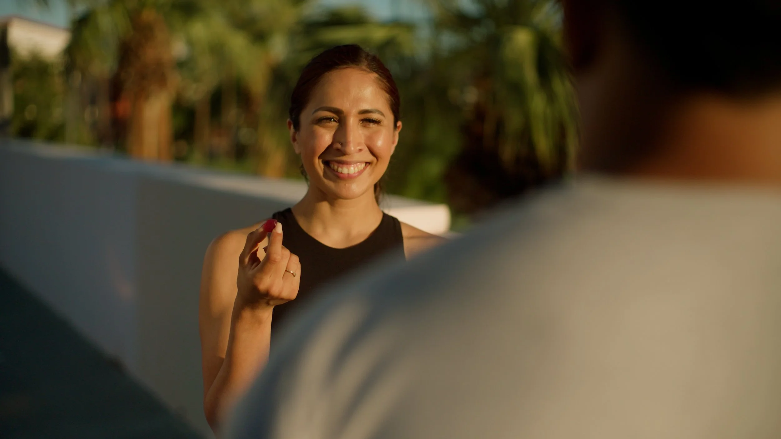 Woman smiling outdoors, holding a small object in hand