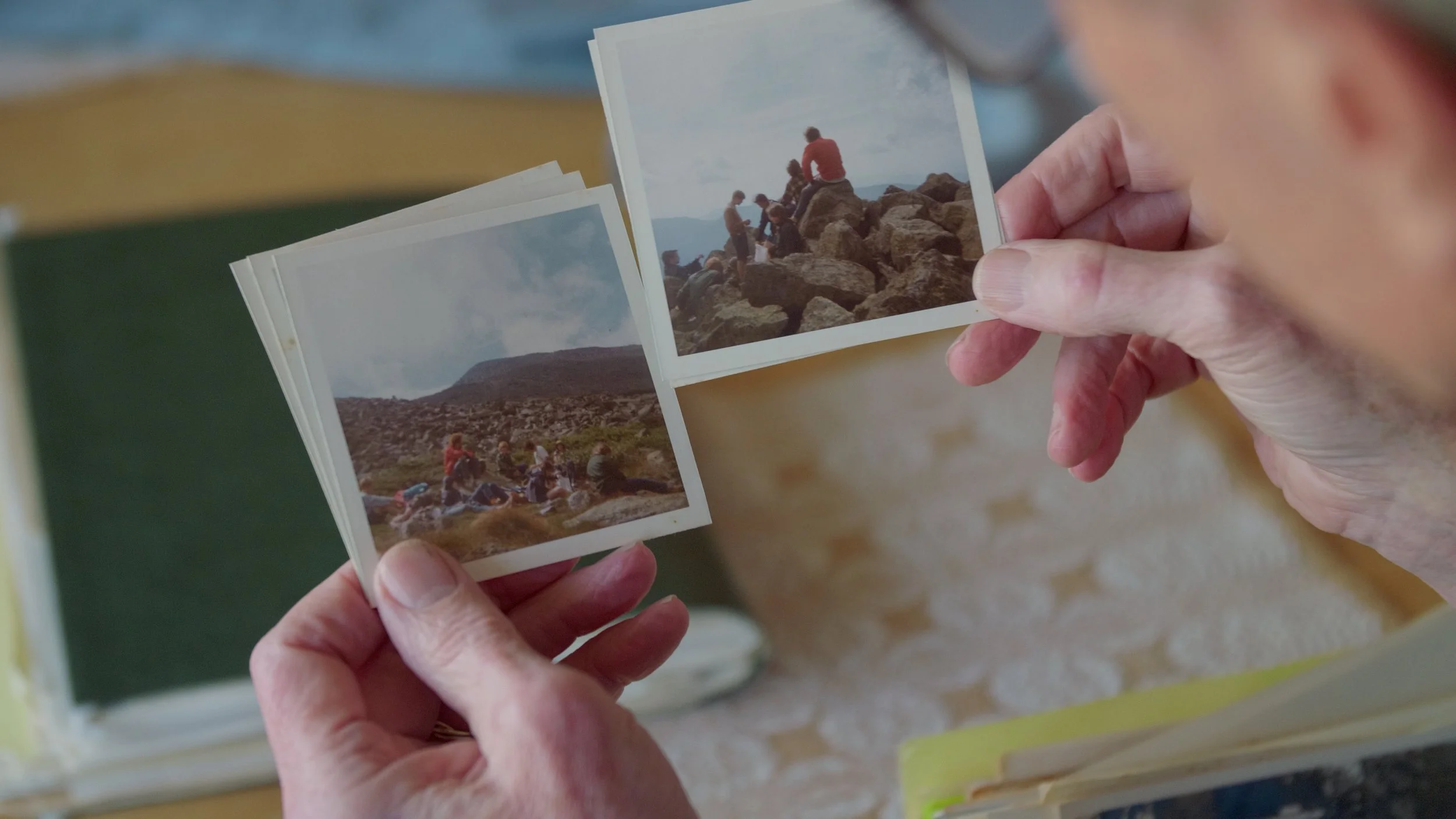 Person holding vintage color photographs of people on rocky terrain outdoors.
