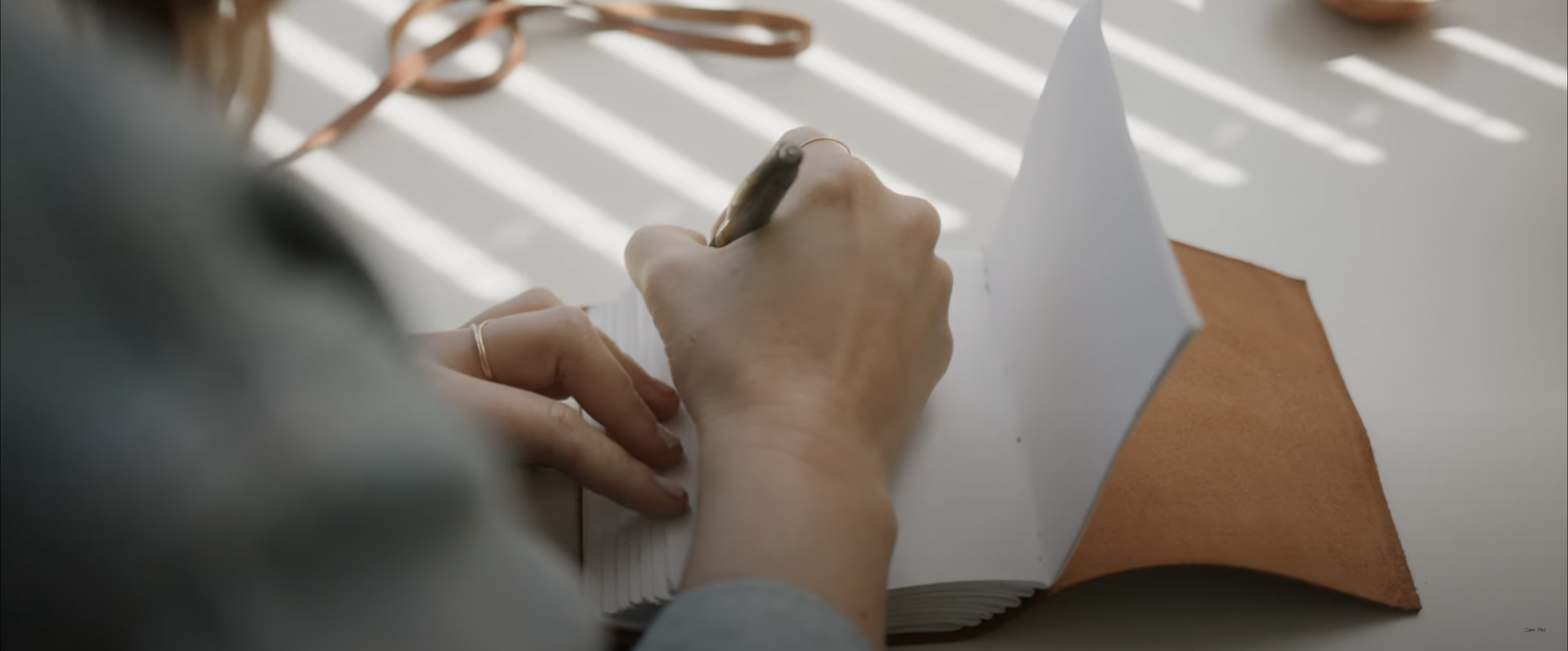 Person writing in a journal with a brown cover