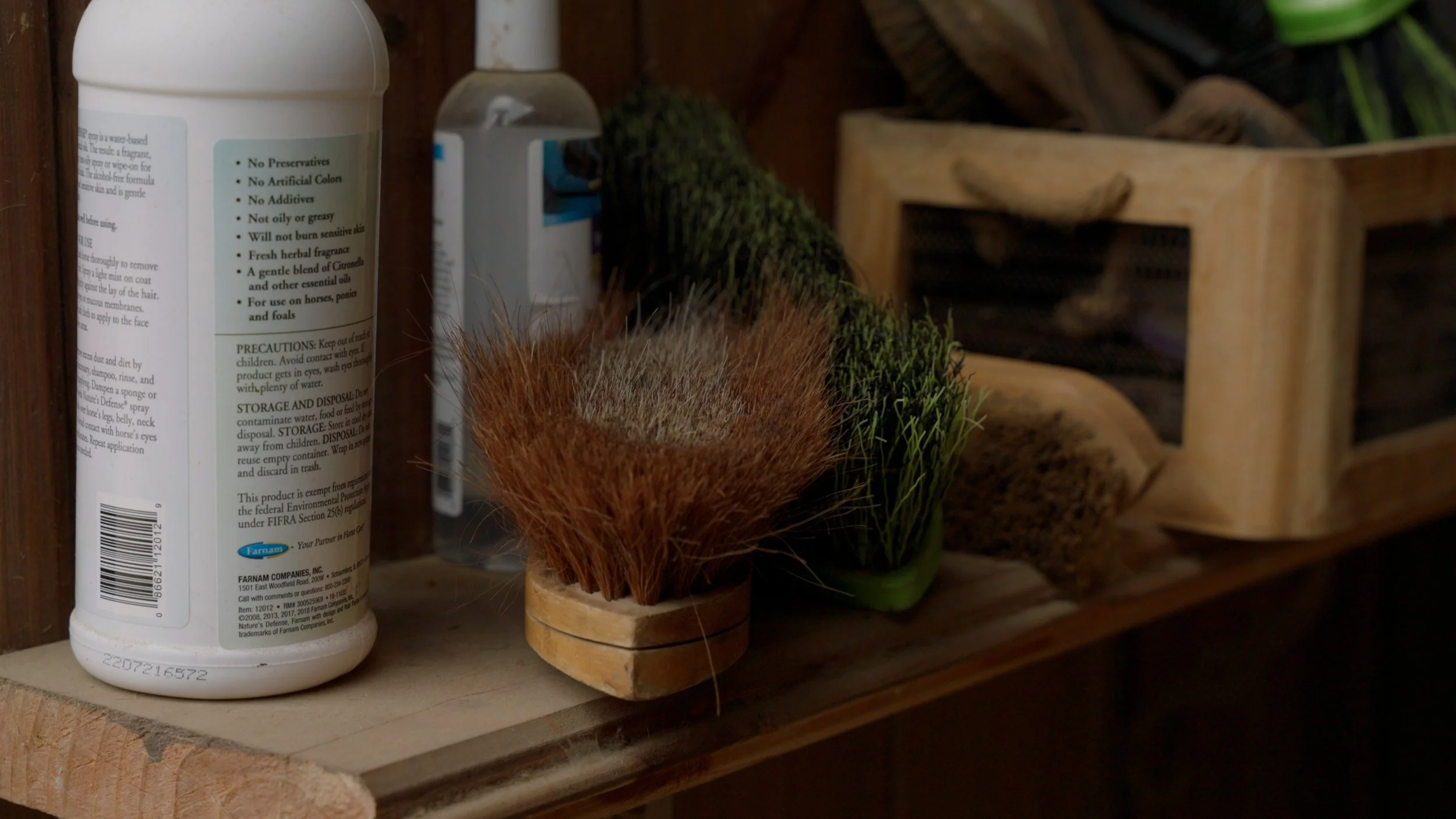 Horse grooming supplies including a bottle of product and various brushes on a wooden shelf.