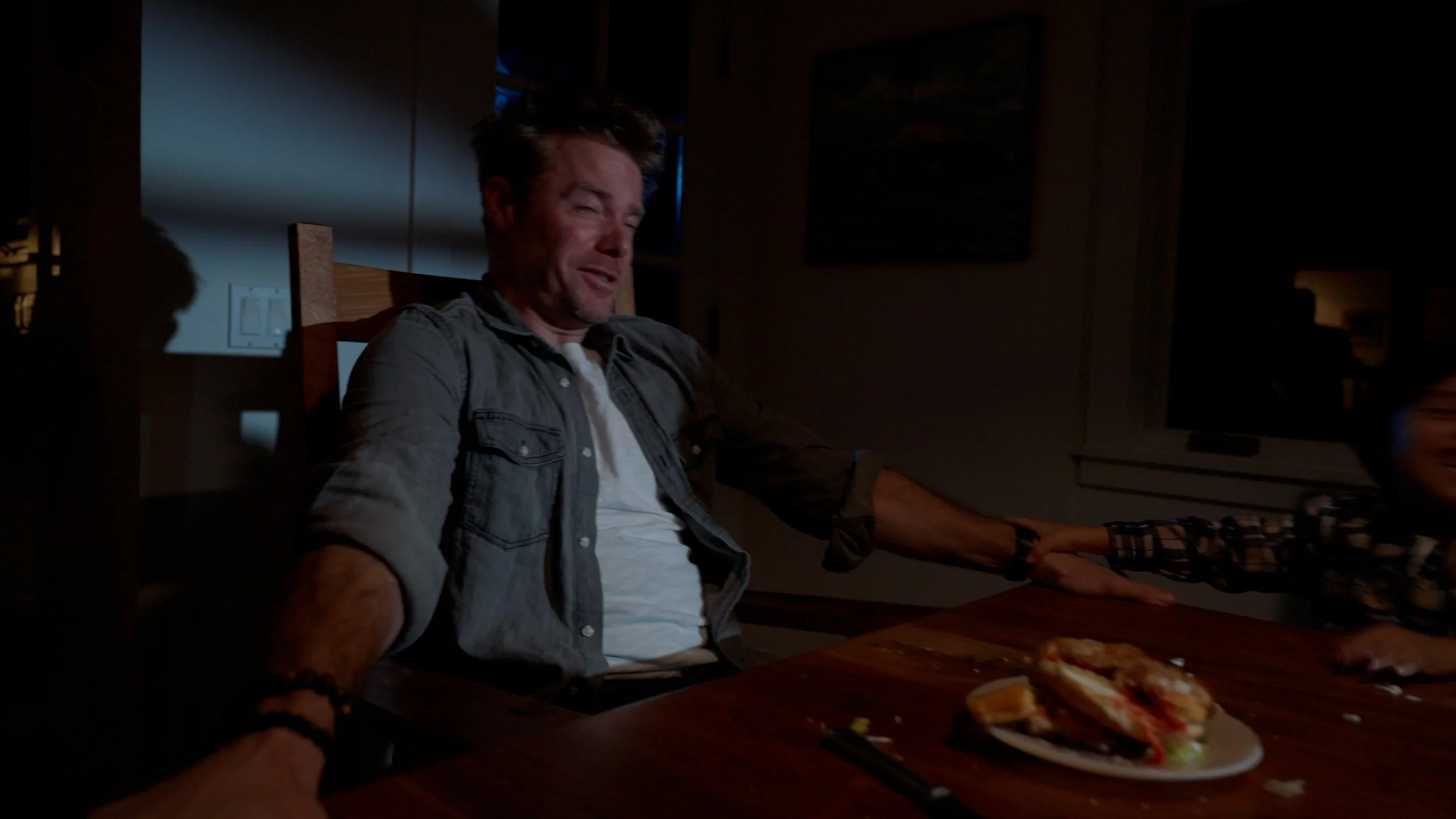 Person sitting at a table in dim lighting with sandwiches on a plate.