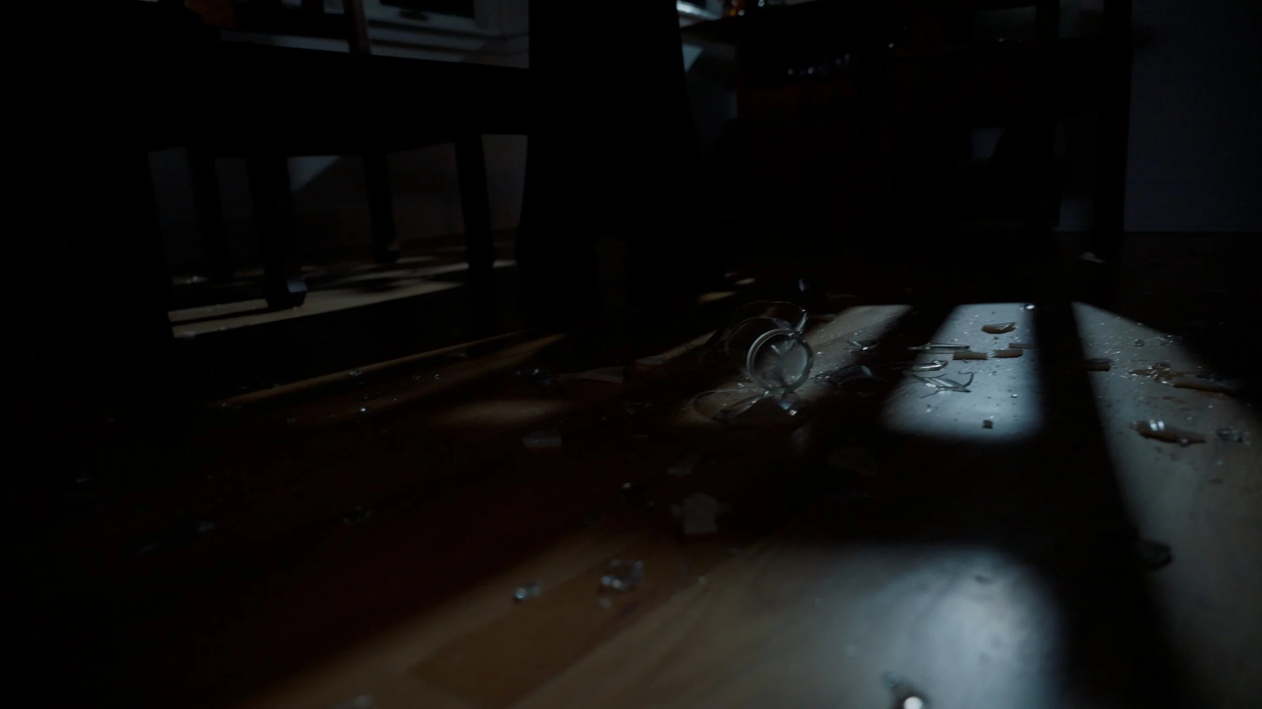 Dimly lit room with broken glass scattered on the floor near shadows.