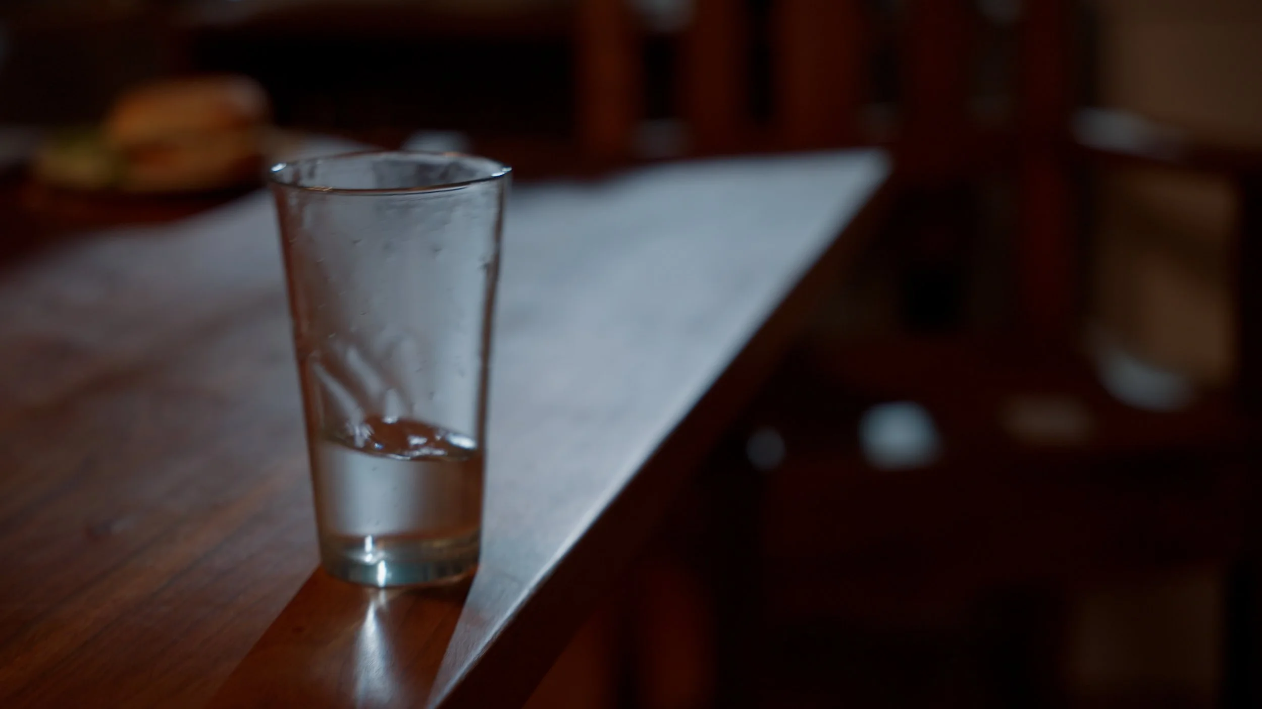 A half-full glass of water on a wooden table with blurred background.