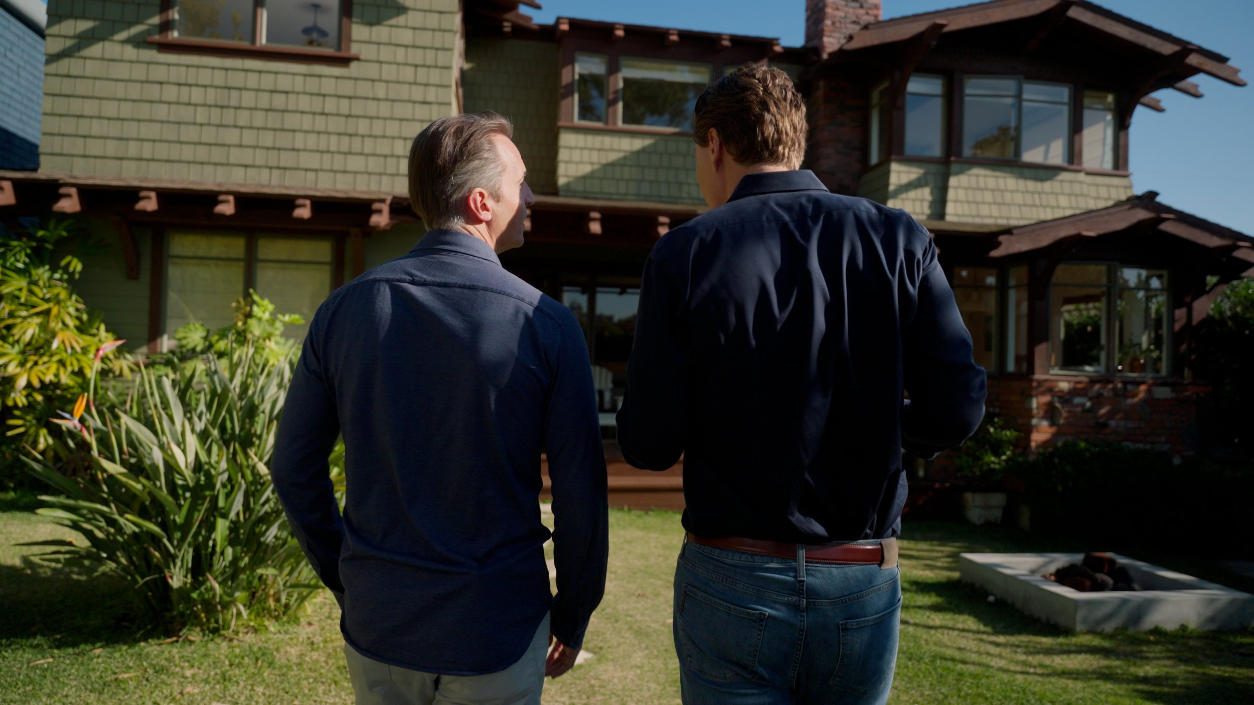 Two men standing in front of a craftsman-style house in a garden.