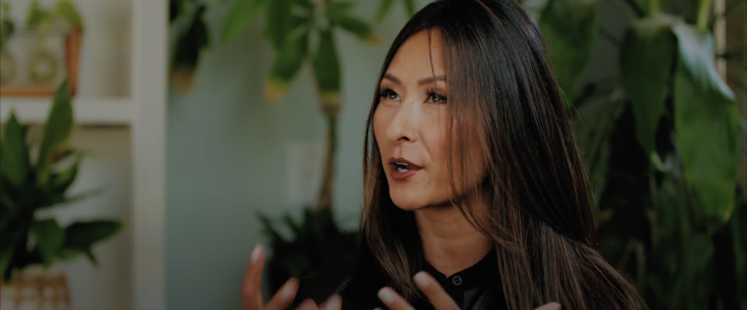 Woman speaking indoors, surrounded by plants
