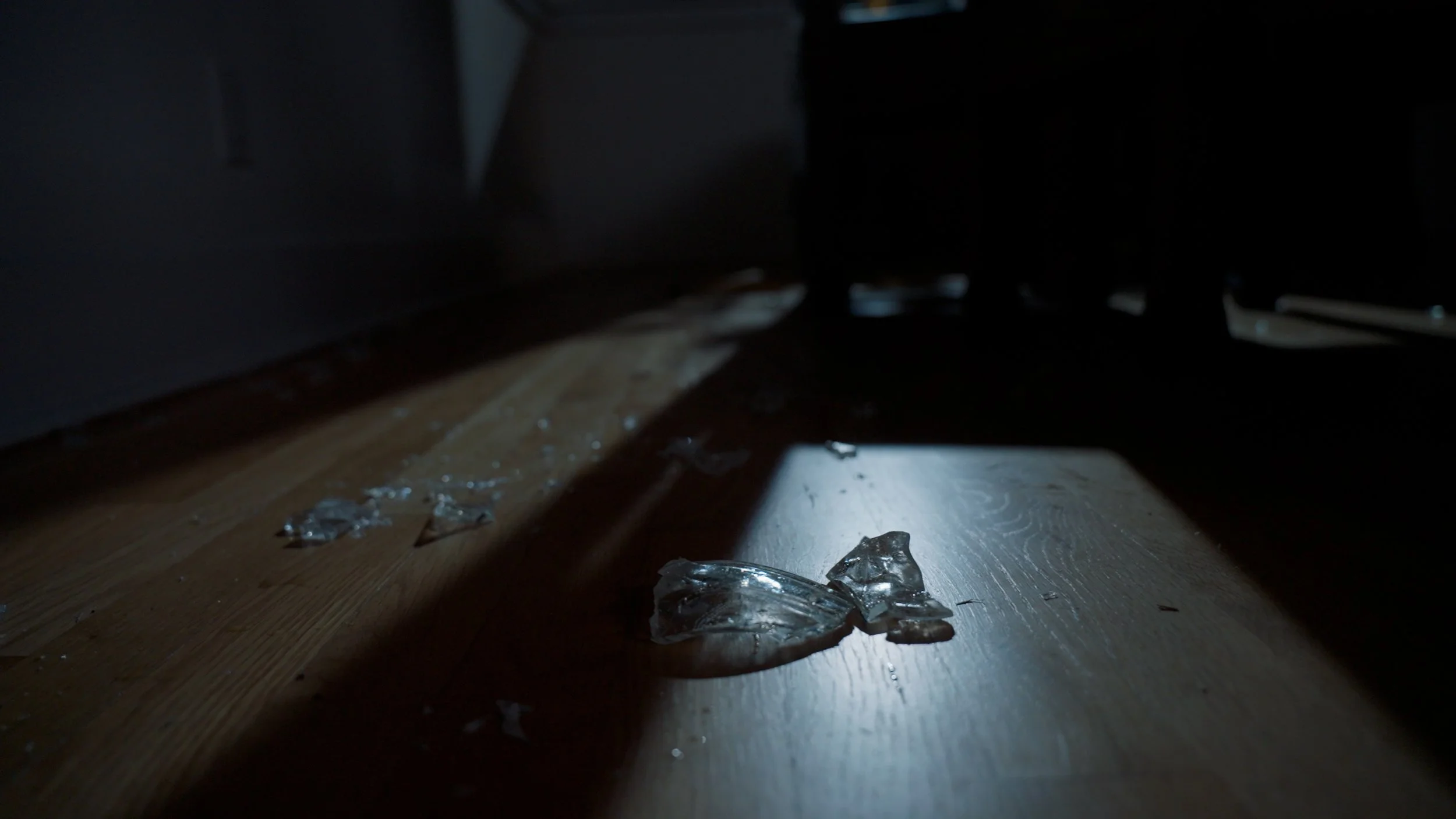 Broken glass pieces on a wooden floor in dim lighting