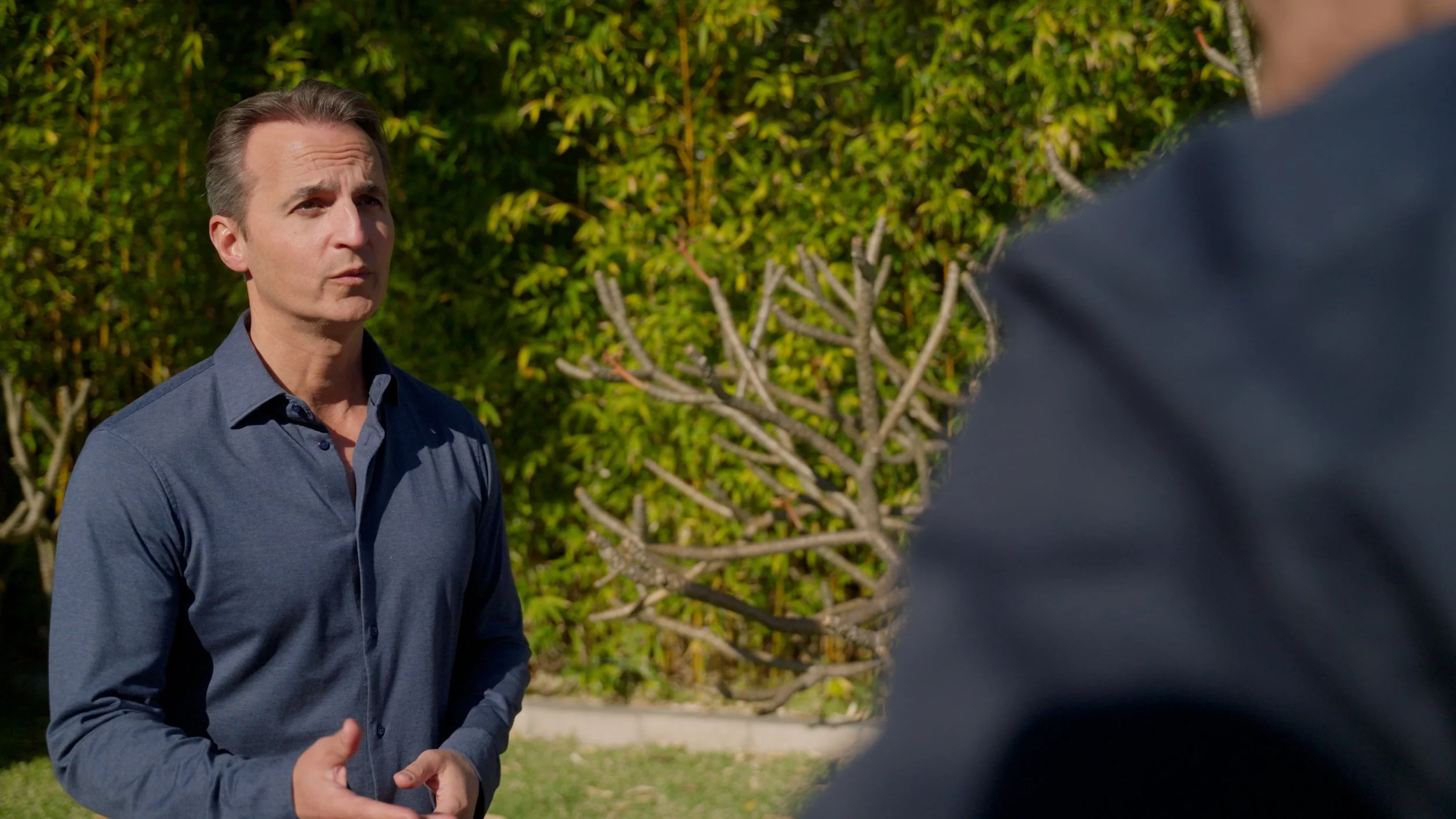 Man in blue shirt standing in garden with tree backdrop
