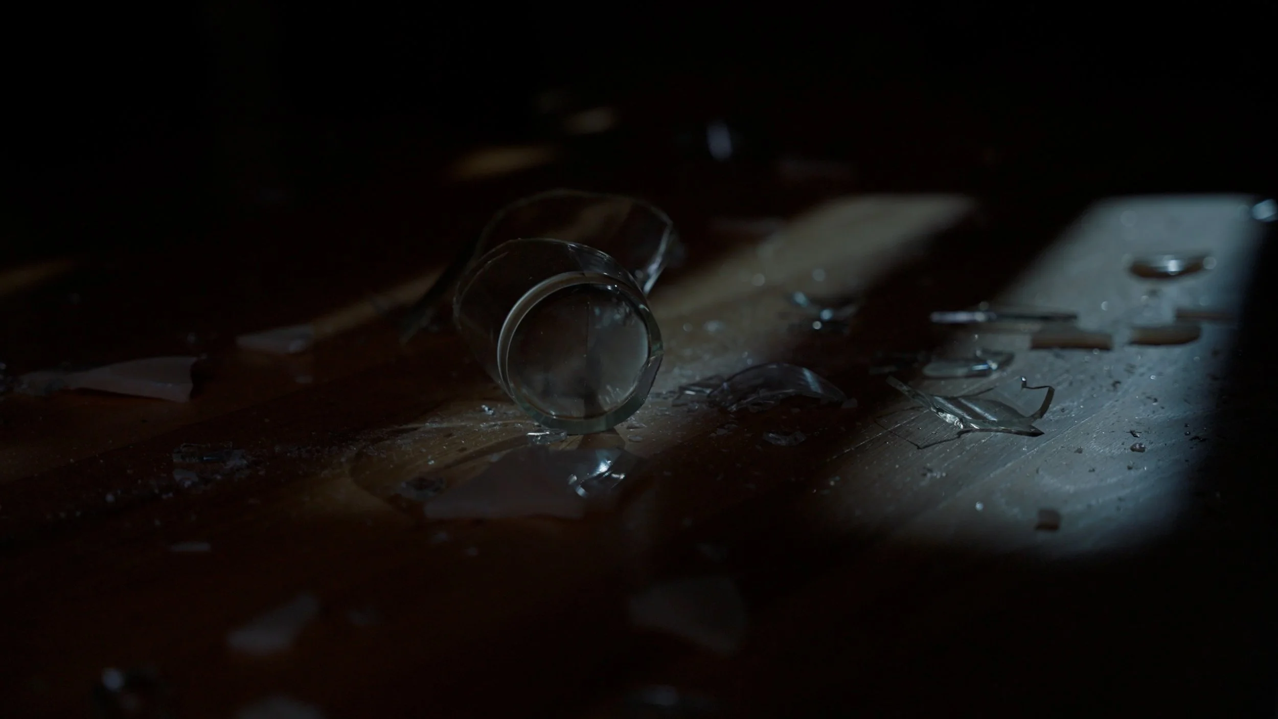 Broken glass bottle on wooden floor with shards scattered