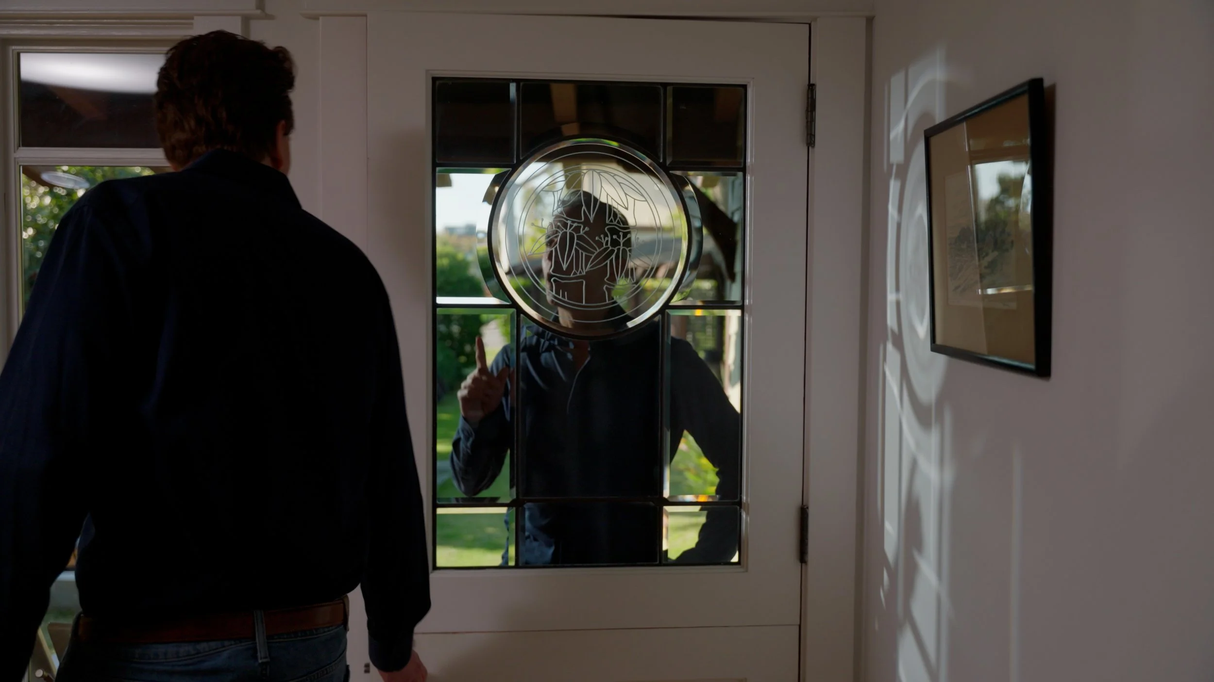 Person opening a door with glass panel reflecting design, man visible outside.