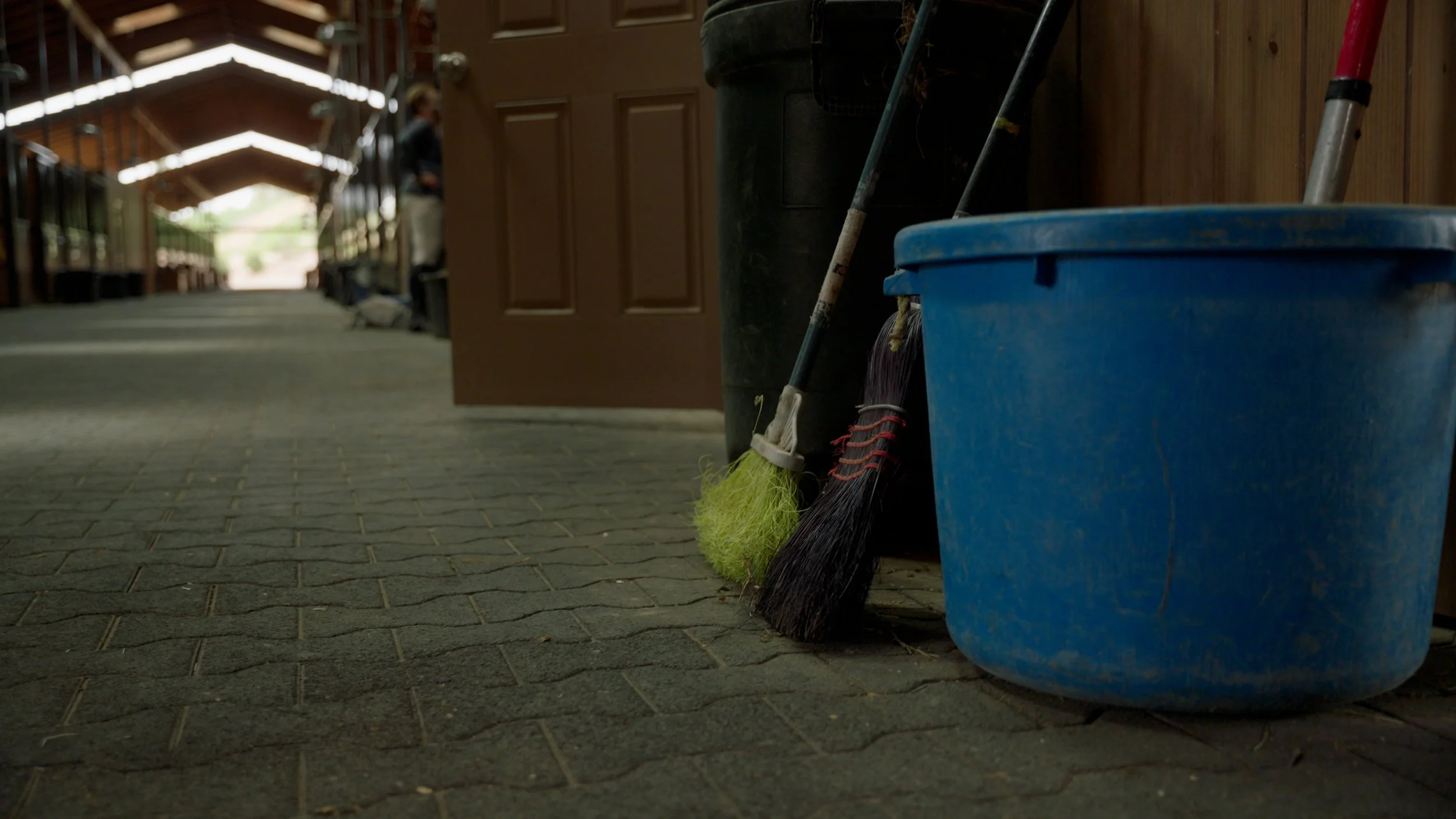 Interior of a barn corridor with cleaning tools and a blue bucket.