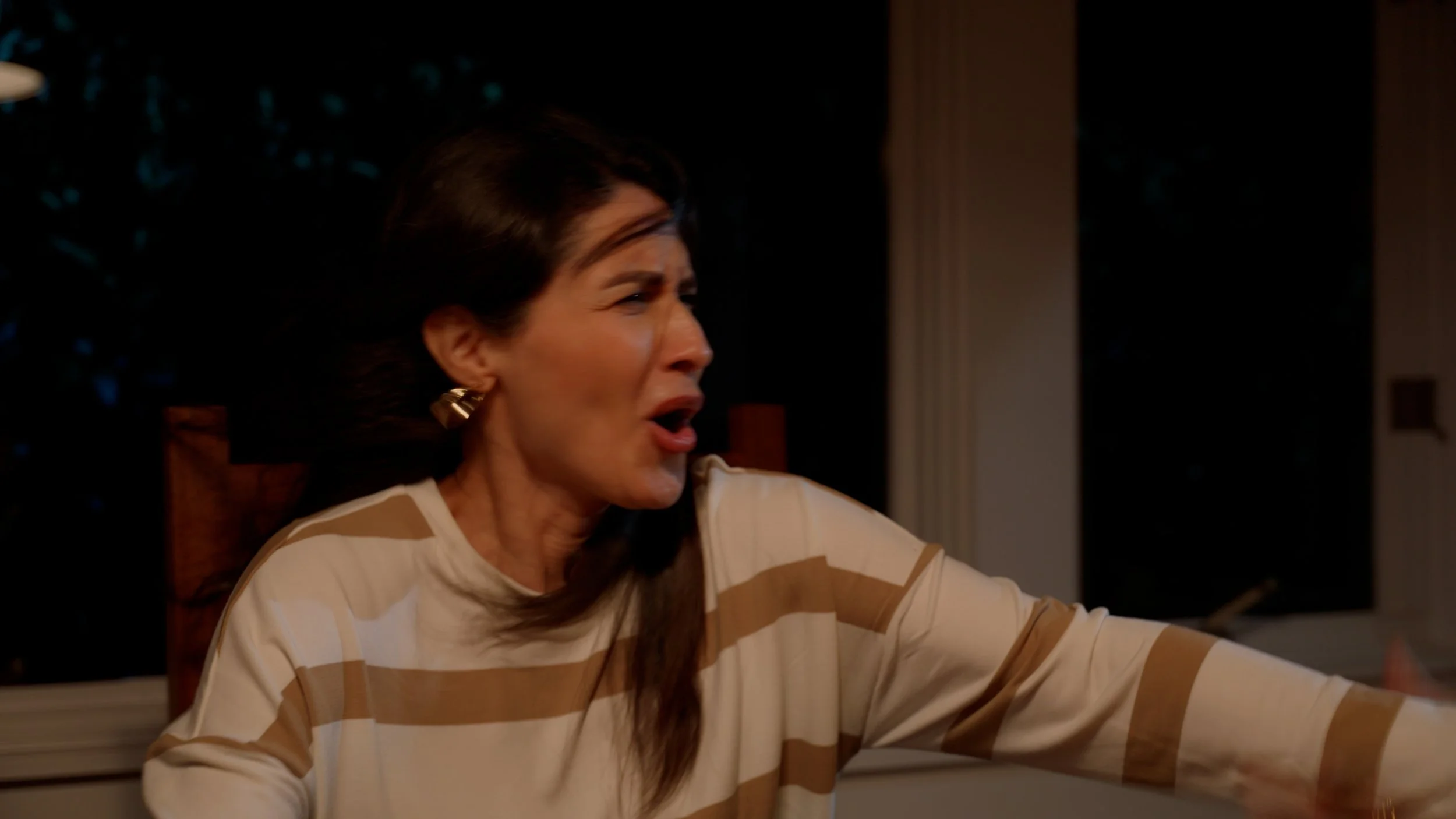 Woman in striped sweater looks surprised, seated indoors.