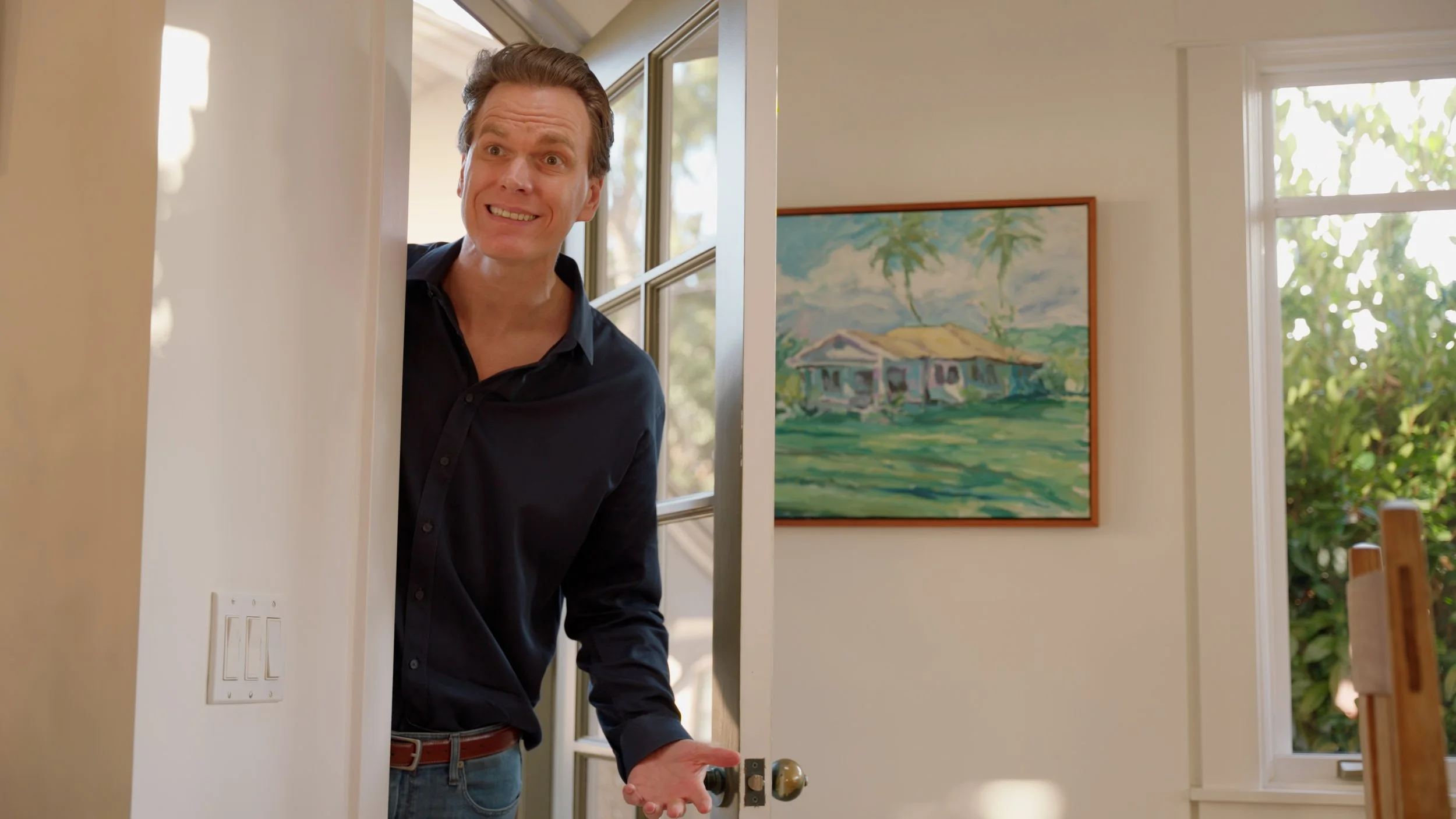 Person in dark shirt standing in doorway, painting of house on wall, interior scene.