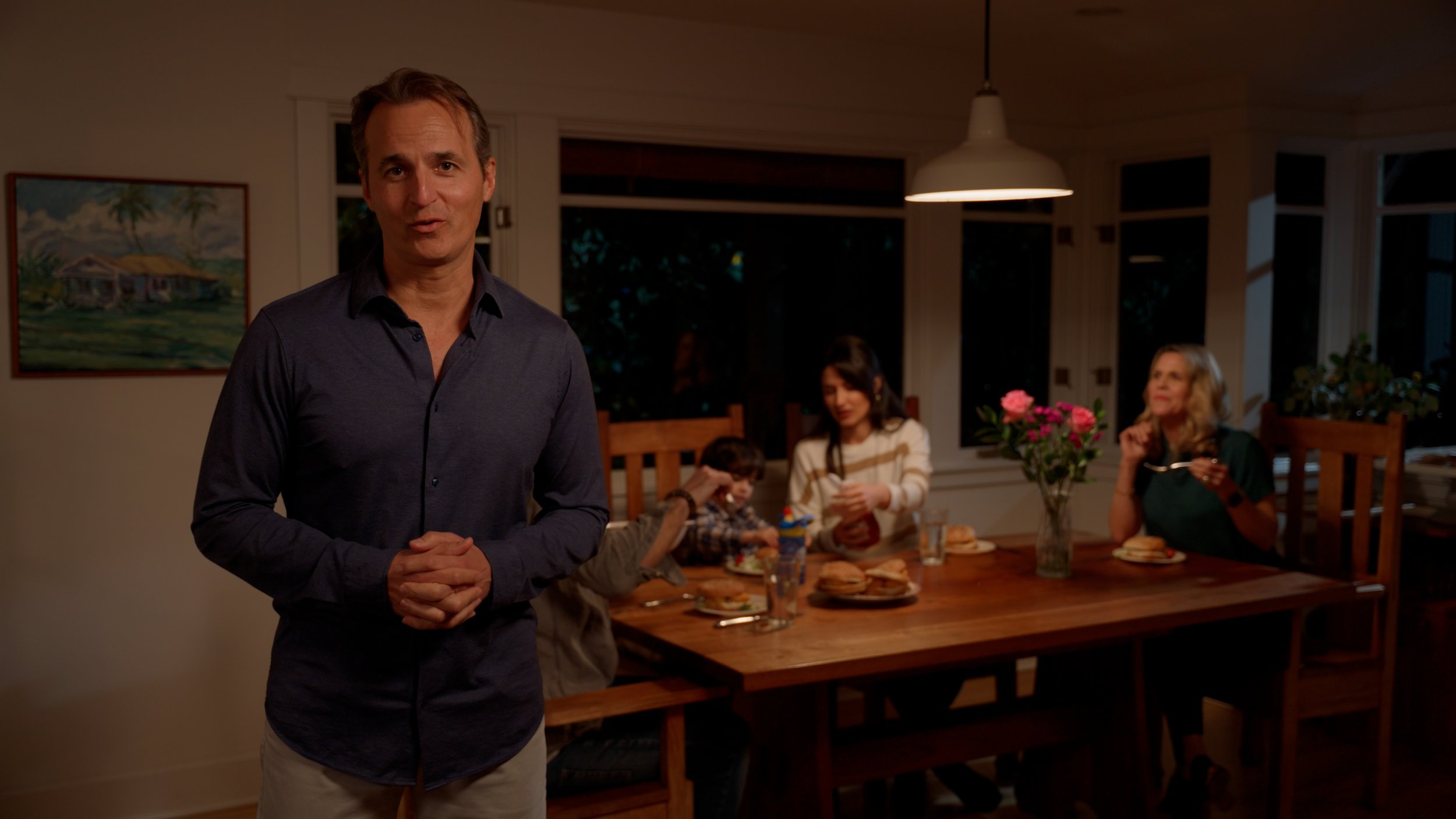 Man standing in front of dining table with people having dinner in a cozy room.