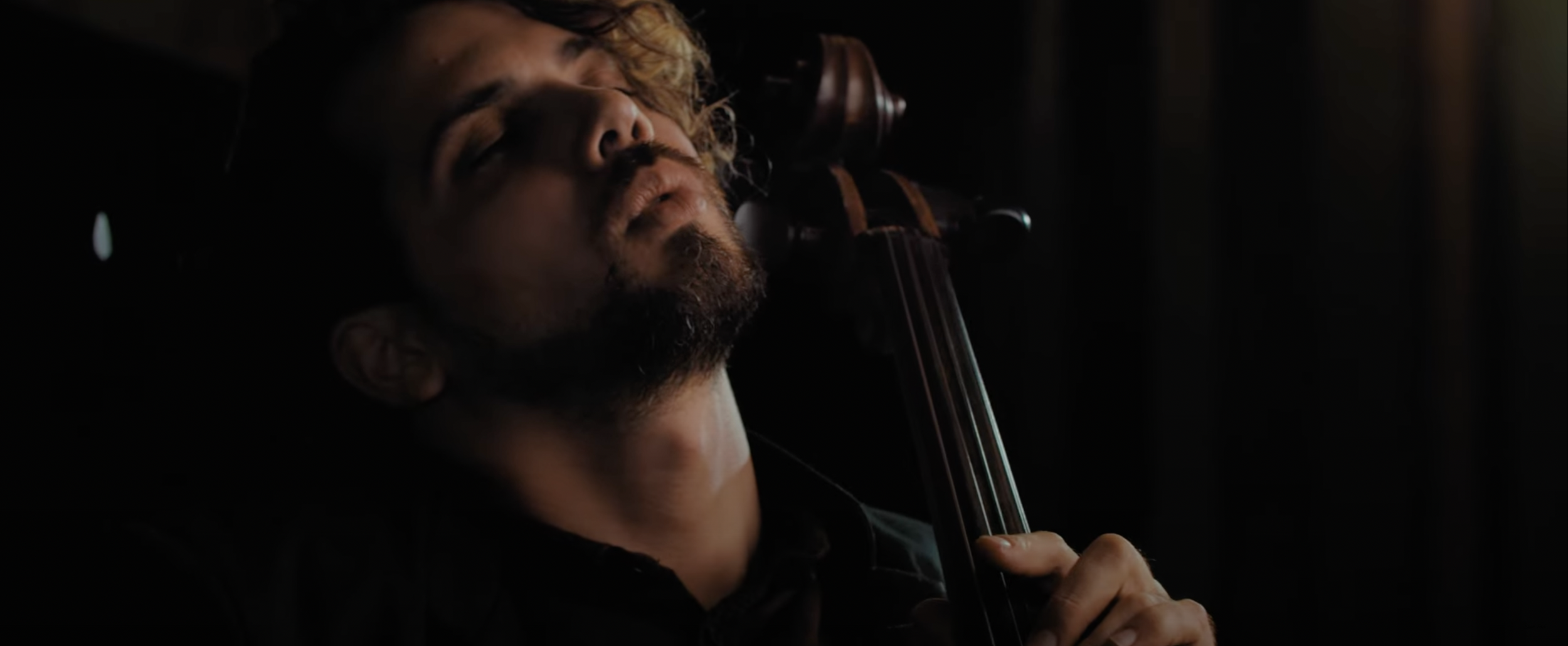 Close-up of a person playing a cello in a dimly lit environment.