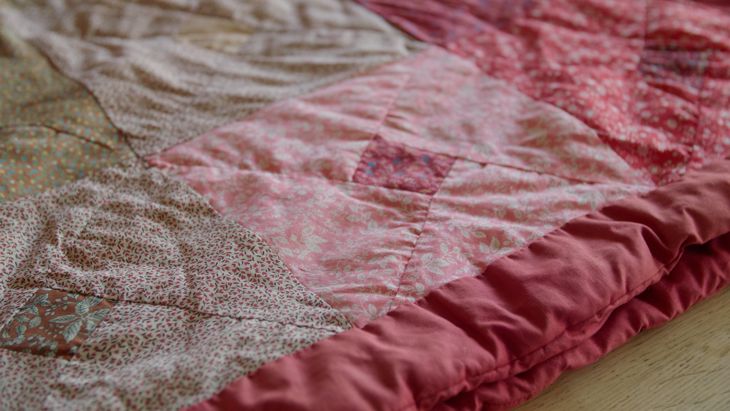 Colorful patchwork quilt with pink, red, and floral patterns on a wooden surface