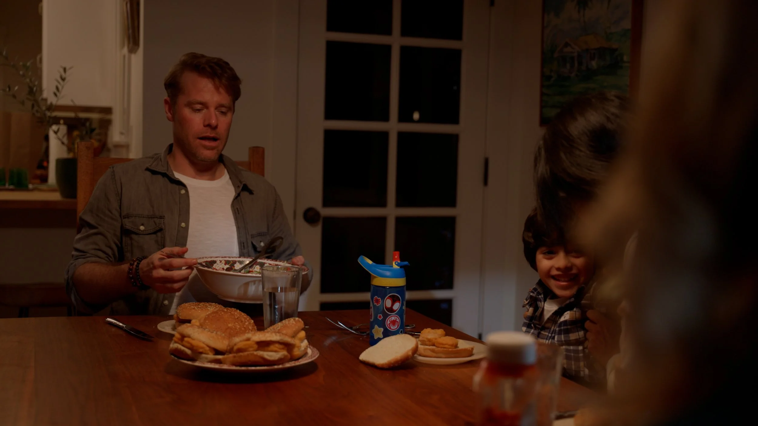 Family dinner scene with man, child, and food on wooden table