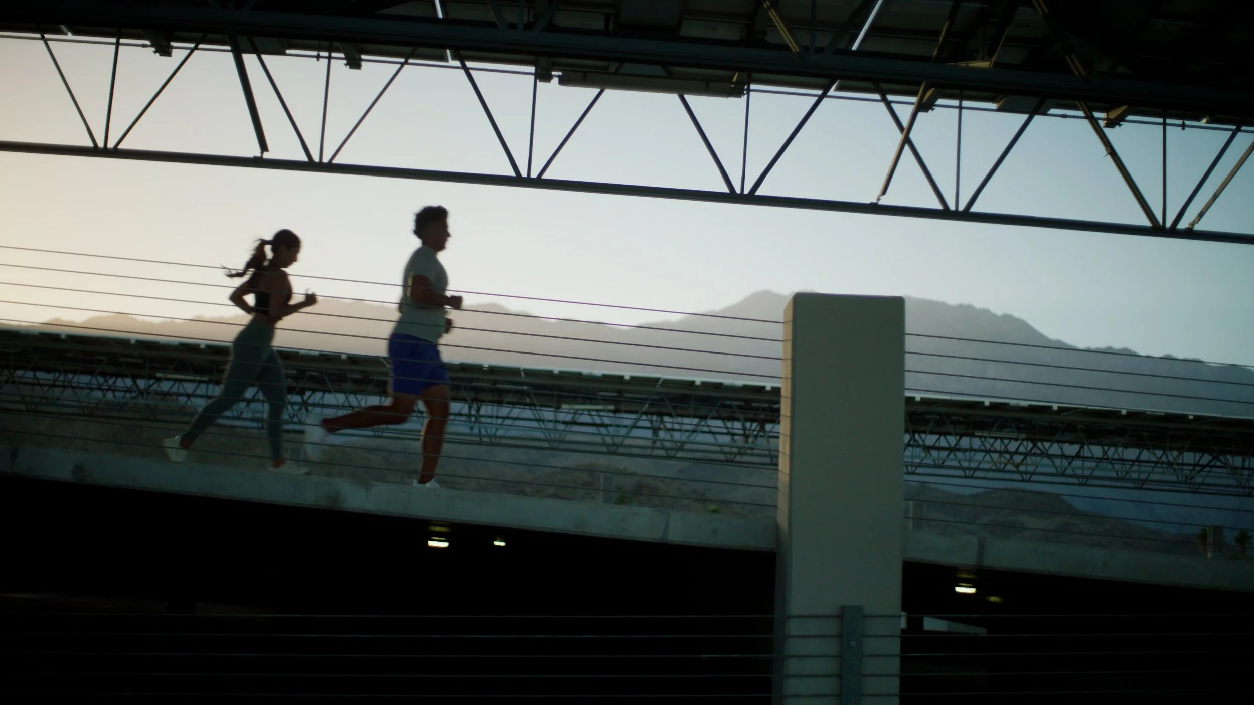 two people jogging on a bridge with mountains in the background
