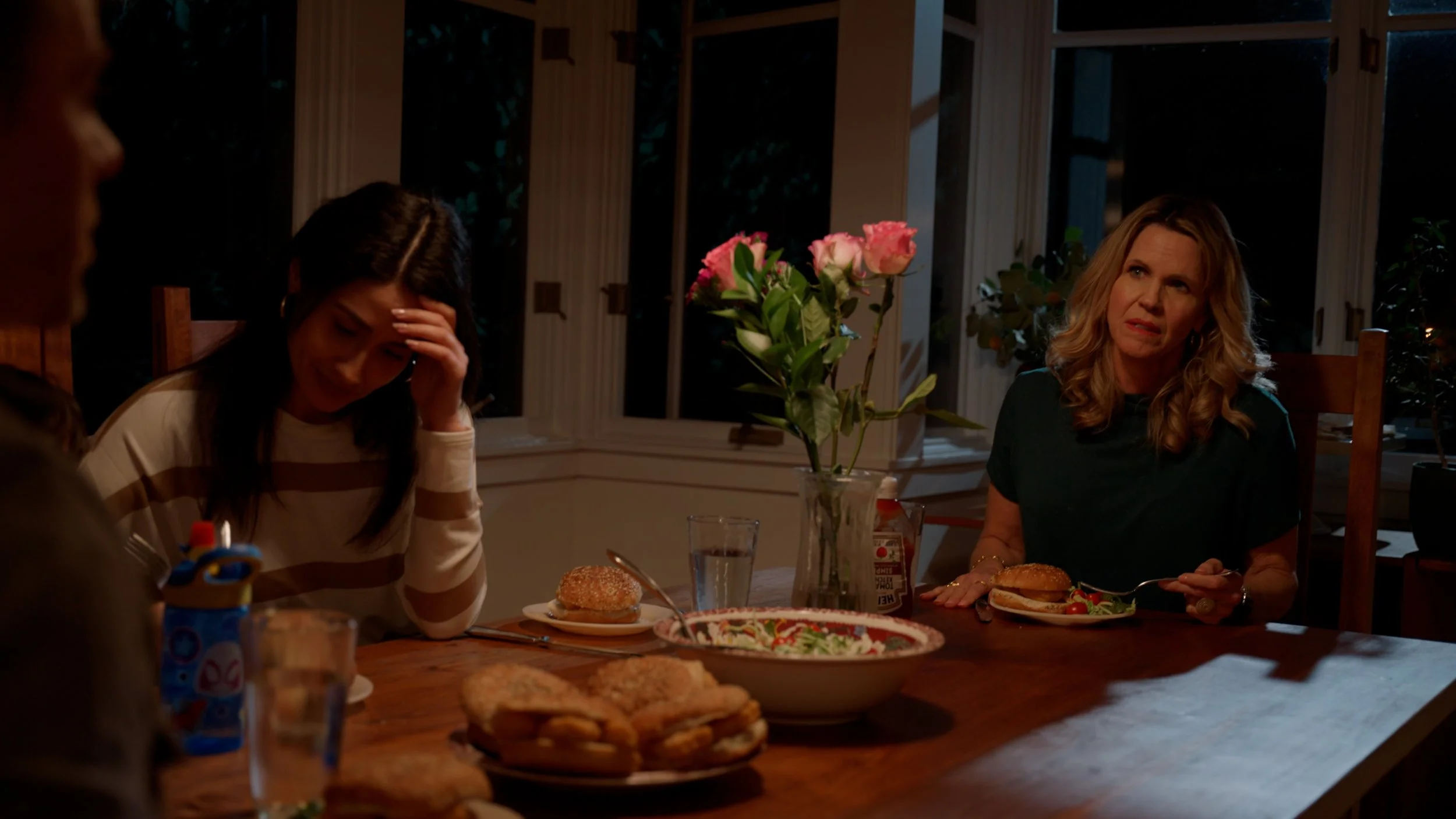 Two women sitting at dining table with burgers and salad