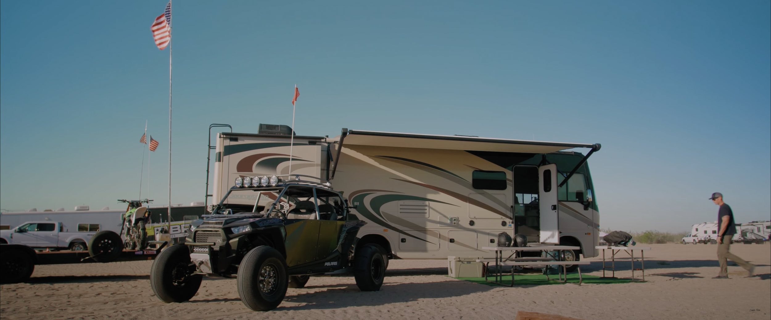 Recreational vehicle with off-road buggy and equipment at a campsite, American flag, desert setting
