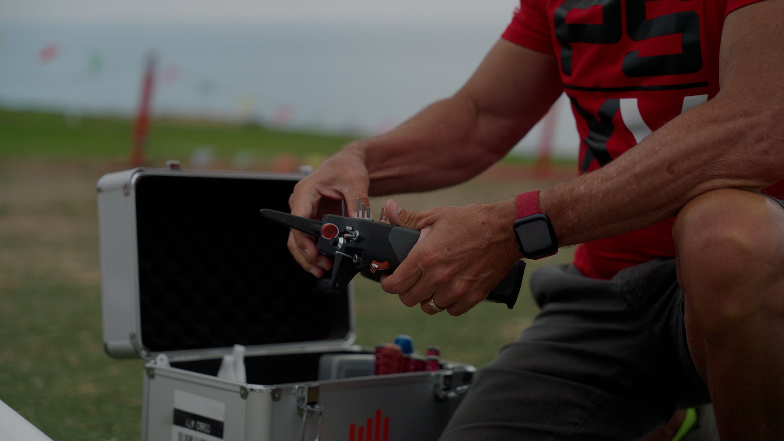 Person holding a black device near an open metal case with equipment, outdoor setting