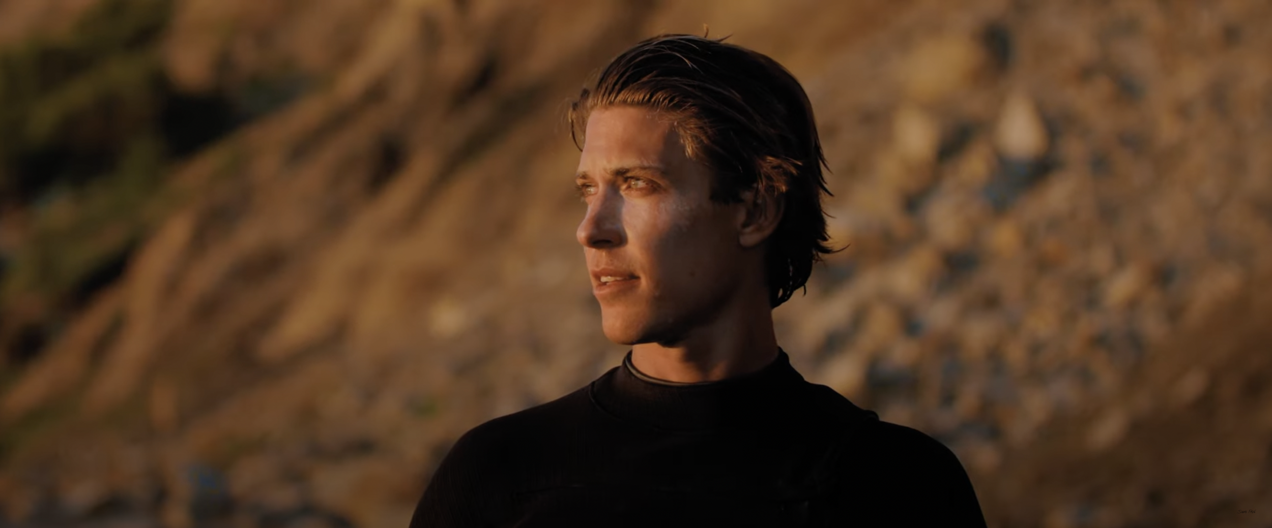 Person in black outfit looking to the side with a rocky background.