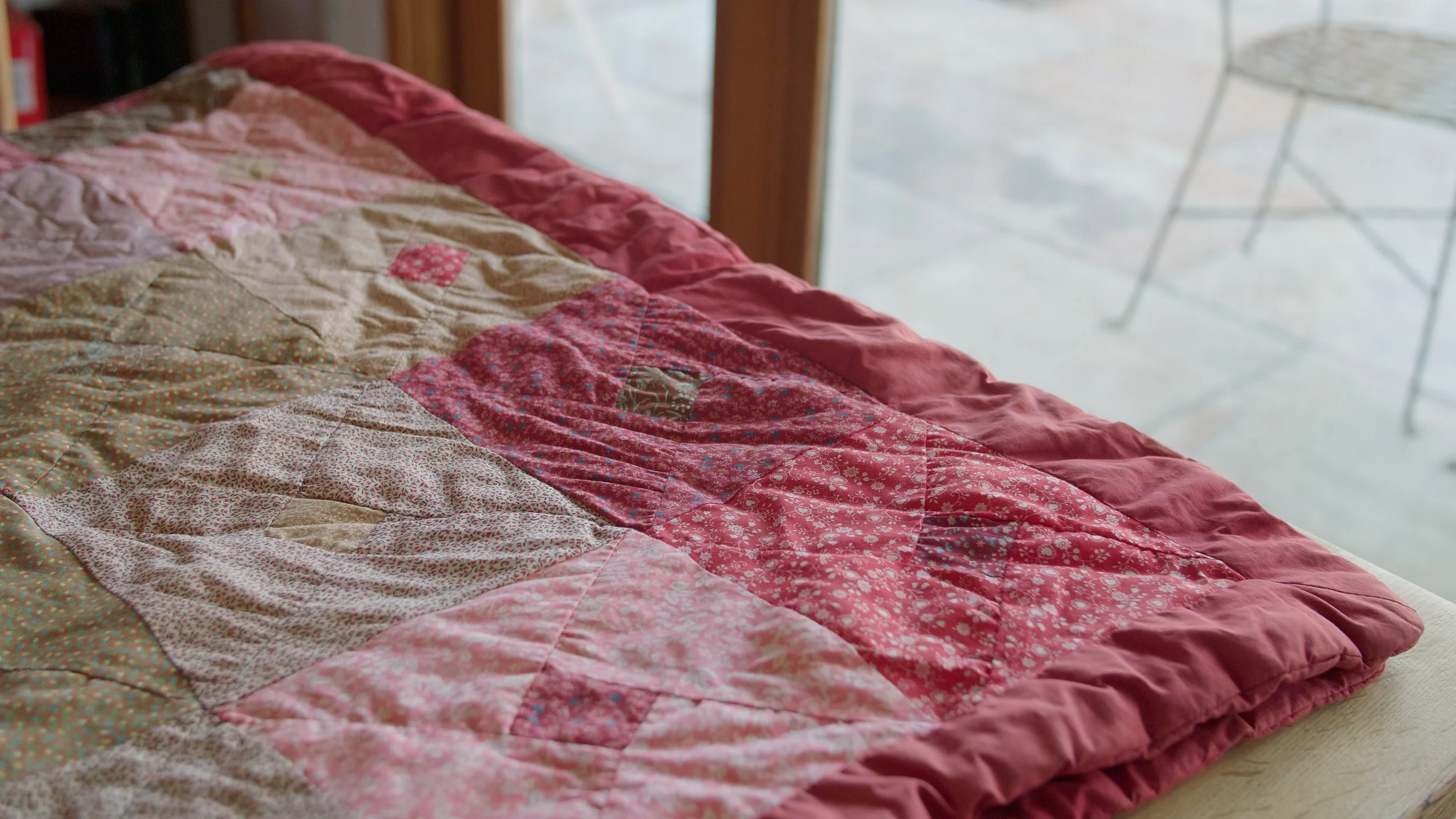 Patchwork quilt with red and pink fabrics on wooden table.