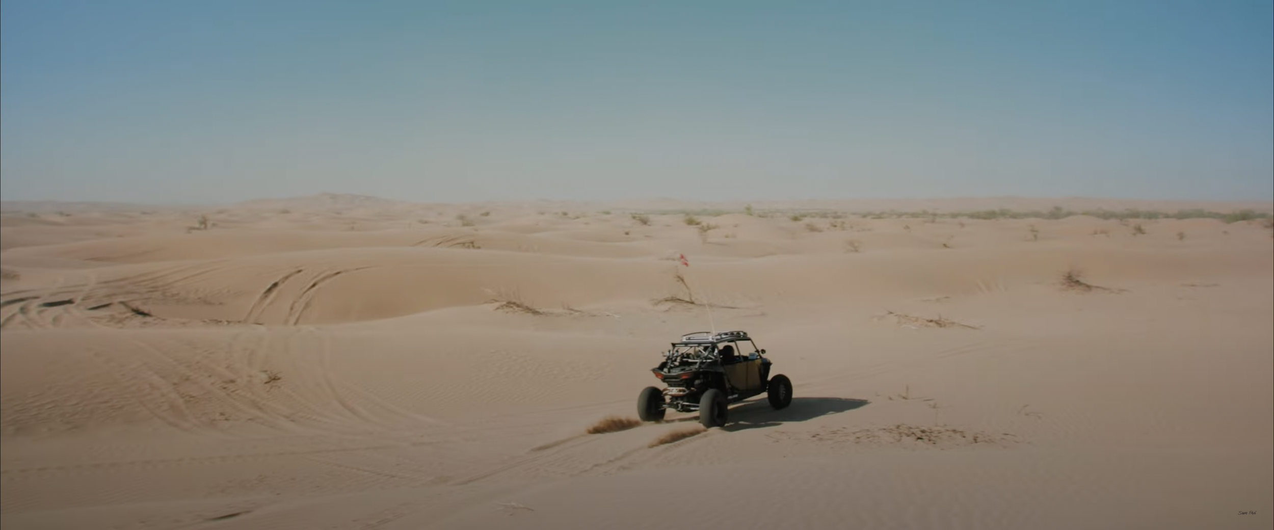 Off-road vehicle driving over sand dunes in a desert landscape