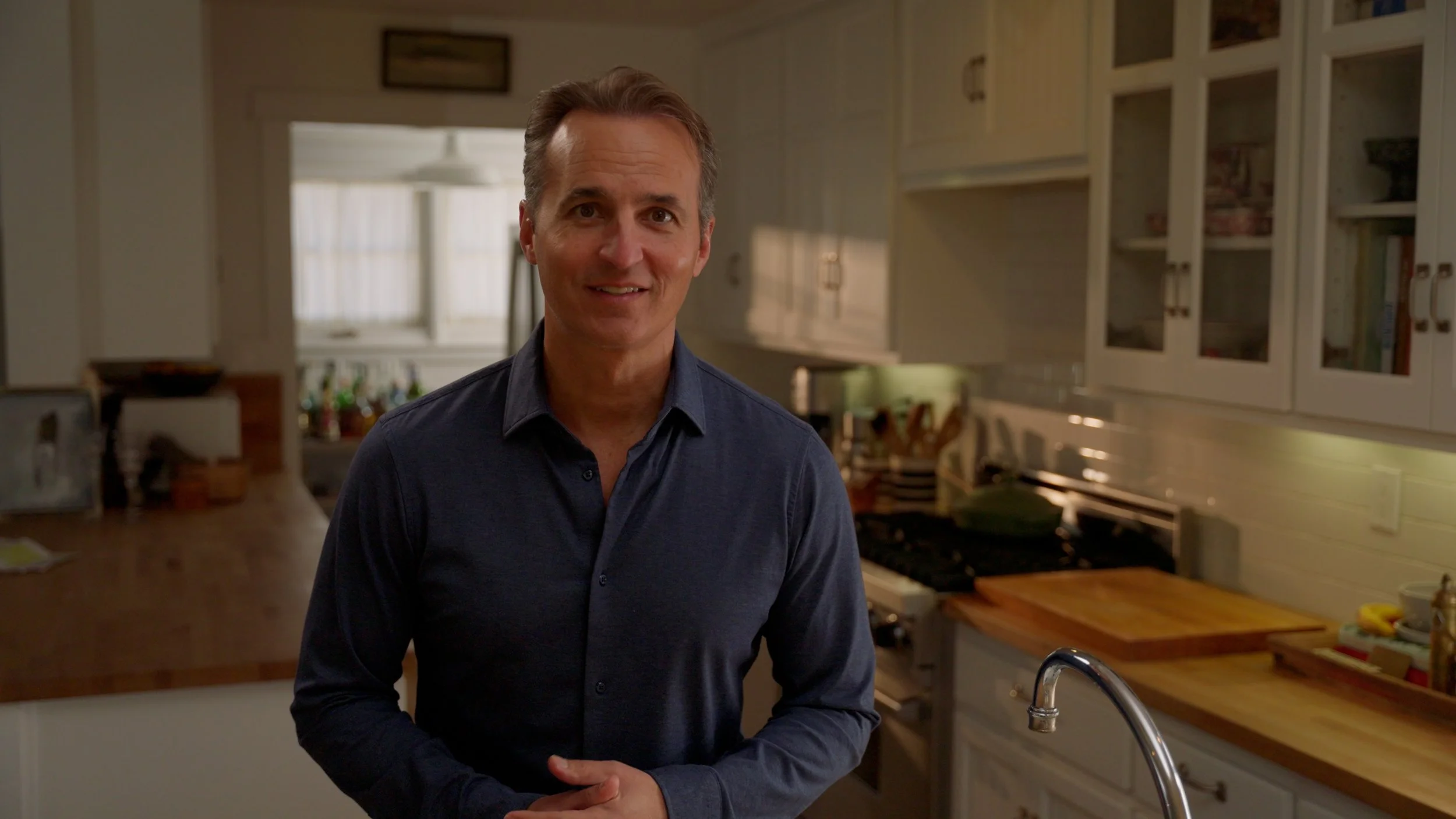 Person smiling in a kitchen with wooden countertops and white cabinets