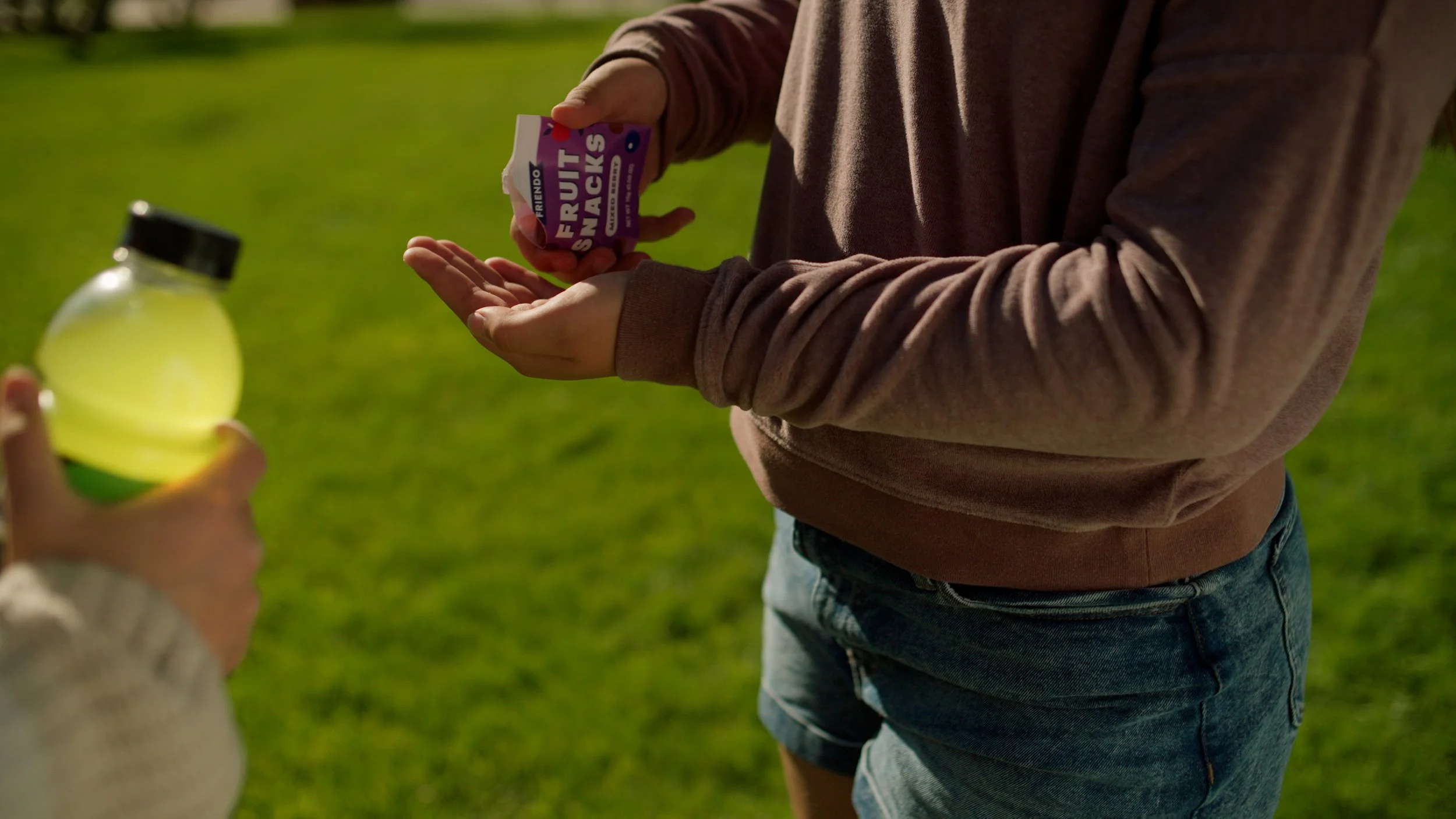 Person holding fruit snacks and drink outdoors