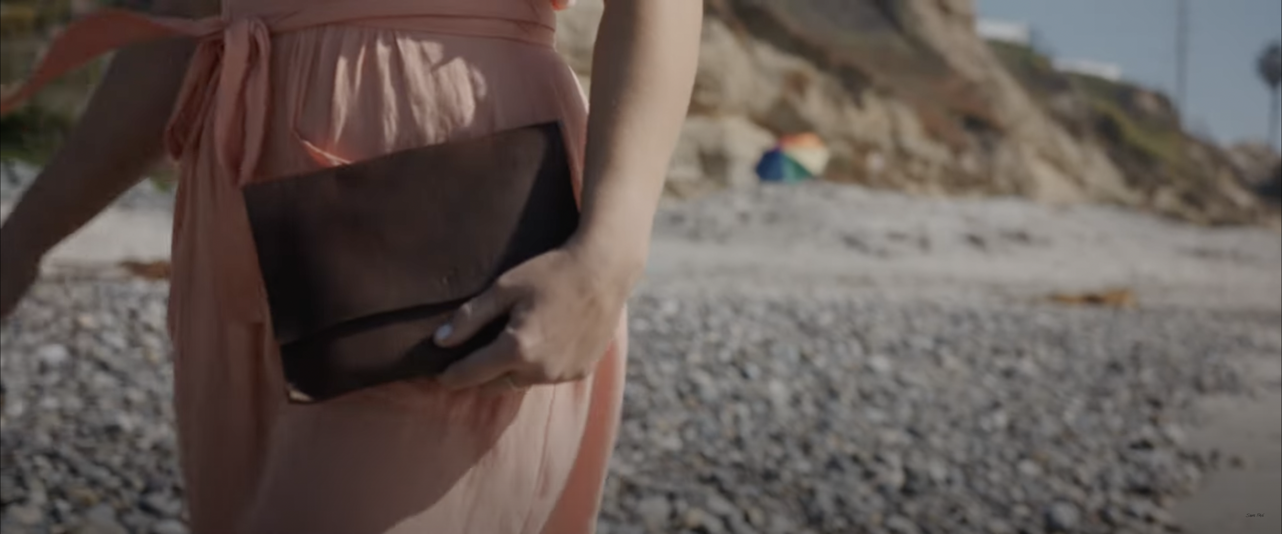 person in pink dress holding a brown clutch walking on a beach
