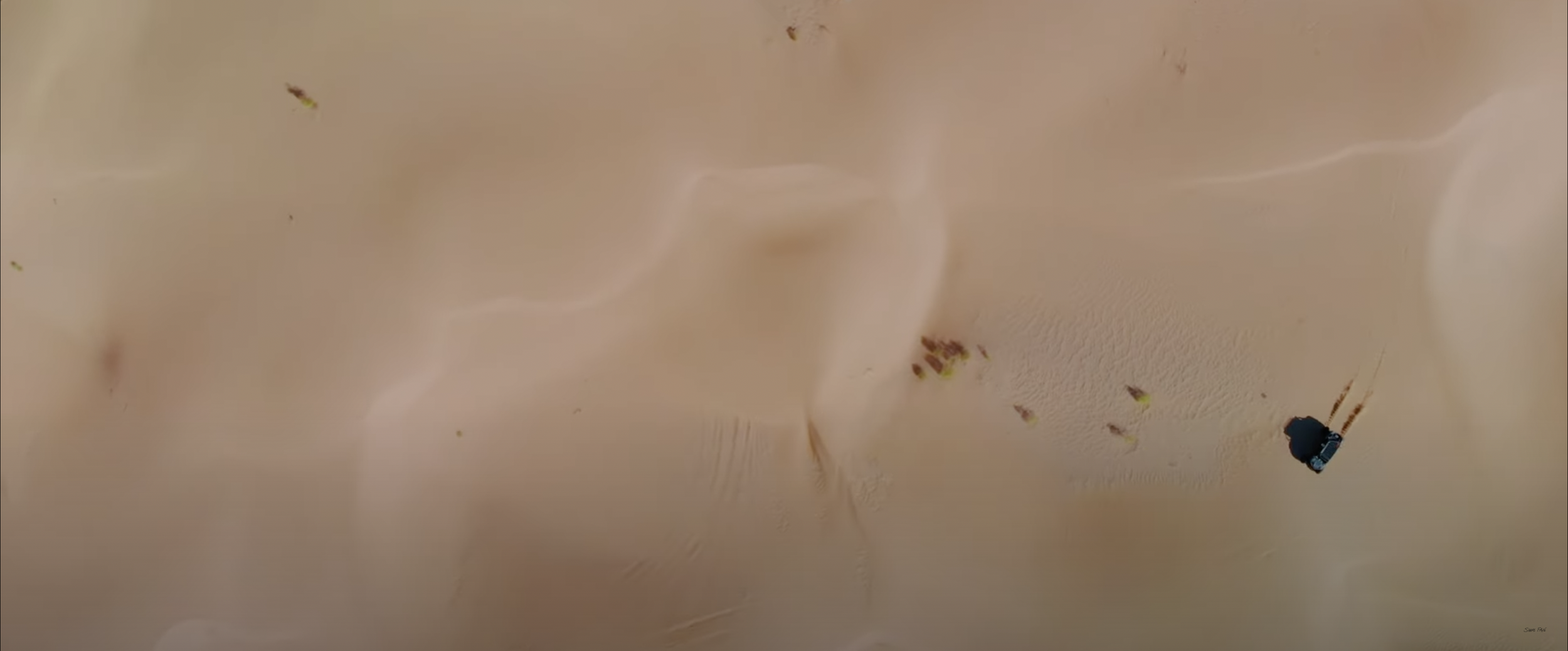 Aerial view of sand dunes with a dark vehicle and scattered vegetation
